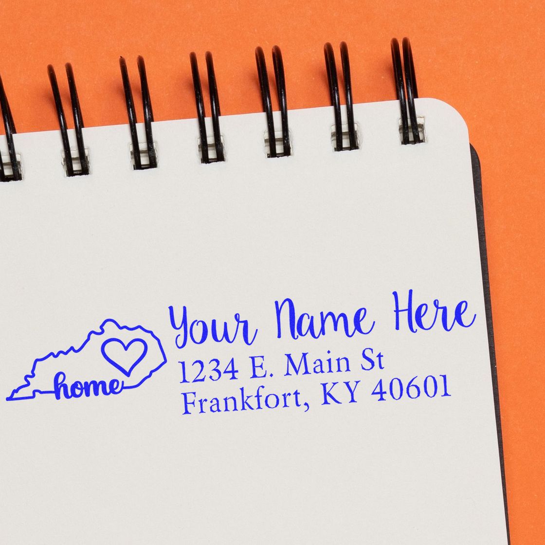 Wood Handle Kentucky Custom Address Rubber Stamp on a spiral notebook, featuring a blue ink design with a heart and state outline, displaying a sample address in Frankfort, KY.