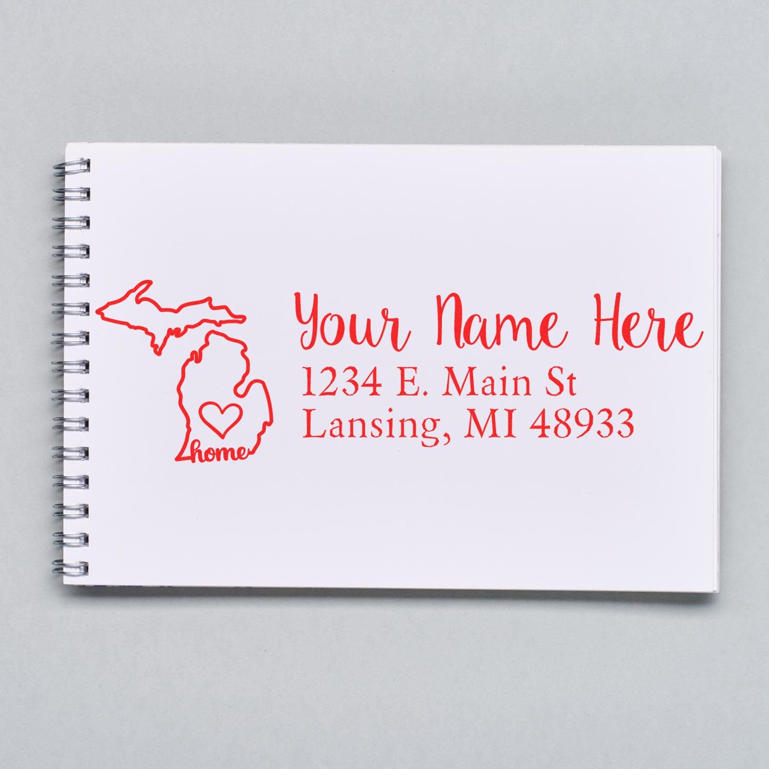 Wood Handle Michigan Custom Address Rubber Stamp on a notebook, featuring a red outline of Michigan with home text and customizable address lines in red script.