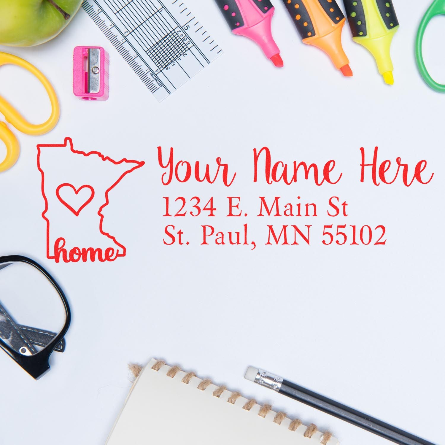 Flat lay of a desk with a Slim Pre-Inked Minnesota State Love Custom Address Stamp impression, featuring a red outline of Minnesota with a heart, surrounded by office supplies like pens and glasses.