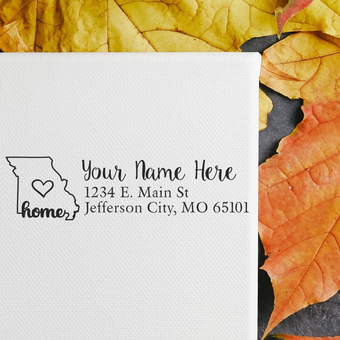 Missouri Self-Inking State Love Address Stamp on white paper with a heart design, surrounded by autumn leaves. Text reads Your Name Here, 1234 E. Main St, Jefferson City, MO 65101.