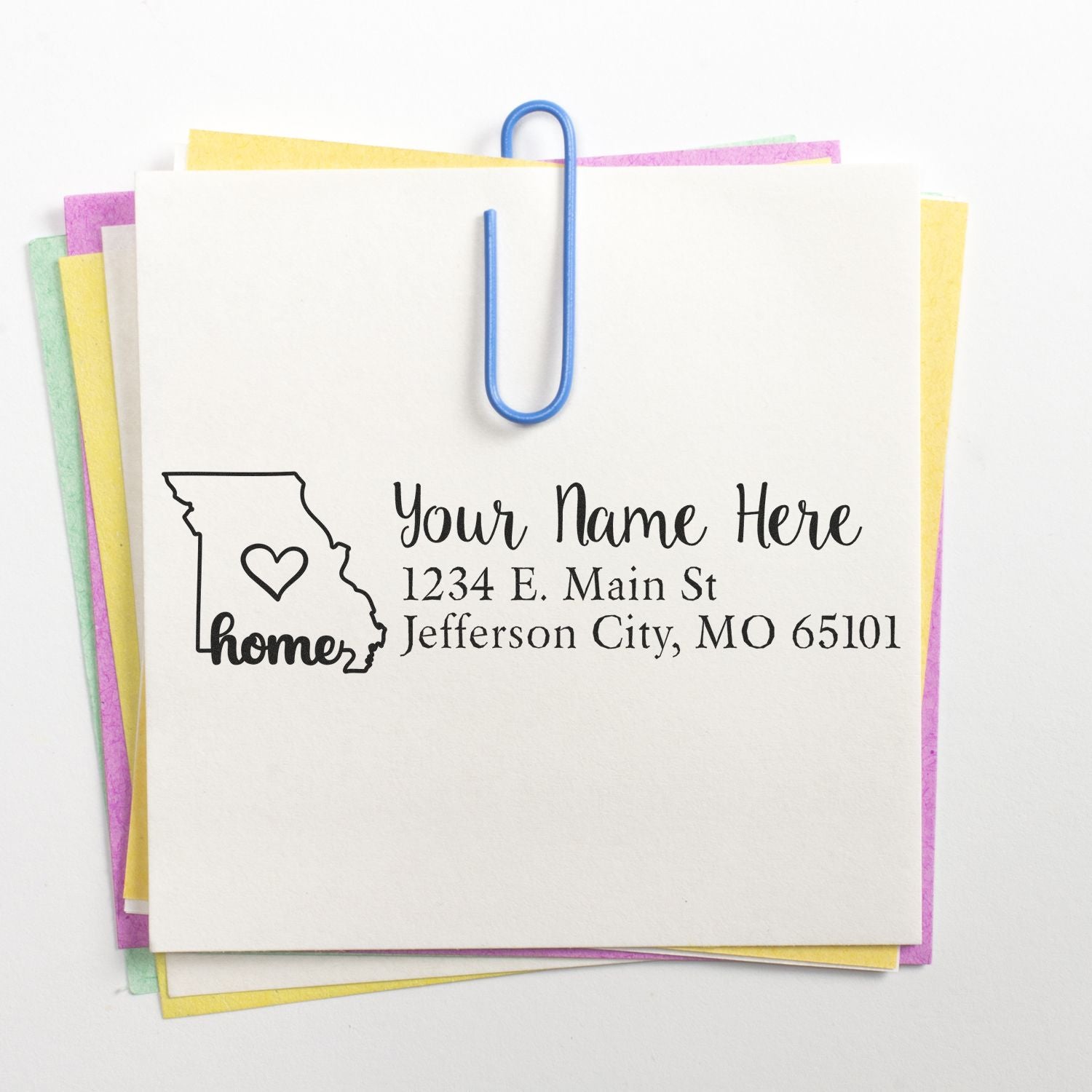 Missouri Self-Inking State Love Address Stamp on a white card with a heart inside the state outline, personalized with Your Name Here and an address, clipped to colorful paper sheets.