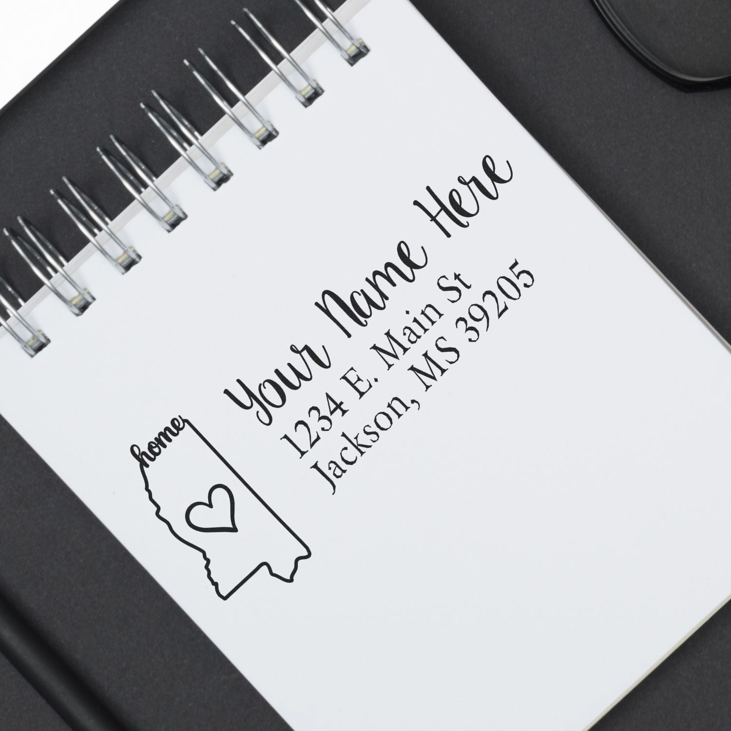 Mississippi Self-Inking State Love Address Stamp on a notebook, featuring a heart and home text with an address in Jackson, MS. Perfect for personalizing mail with a touch of state pride.