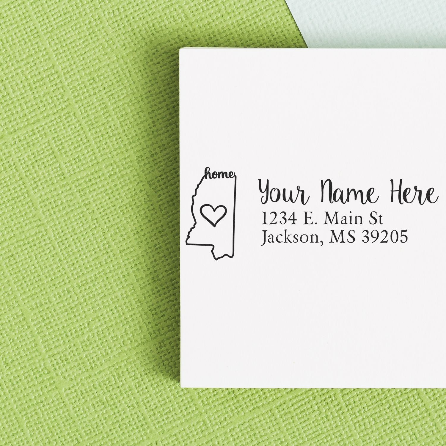 Wood Handle Mississippi Custom Address Rubber Stamp on a white envelope with a green textured background, featuring a heart inside the state outline and customizable address text.