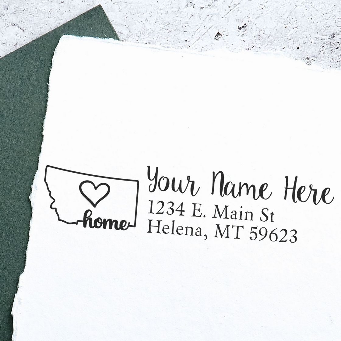 Slim Pre-Inked Montana State Love Custom Address Stamp on white paper, featuring a heart inside the Montana outline with home text, next to a green envelope.