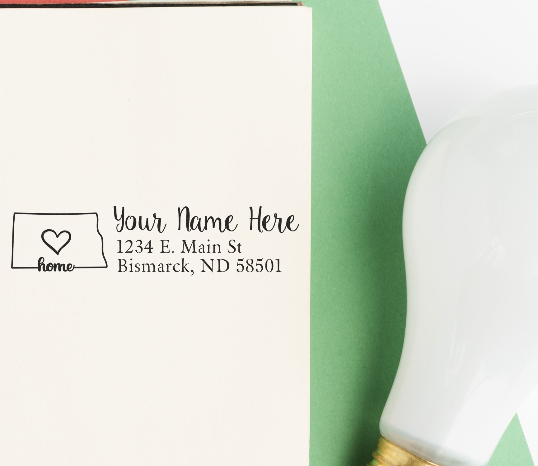 Wood Handle North Dakota Custom Address Rubber Stamp on an envelope with a heart design, next to a green paper and a white light bulb.