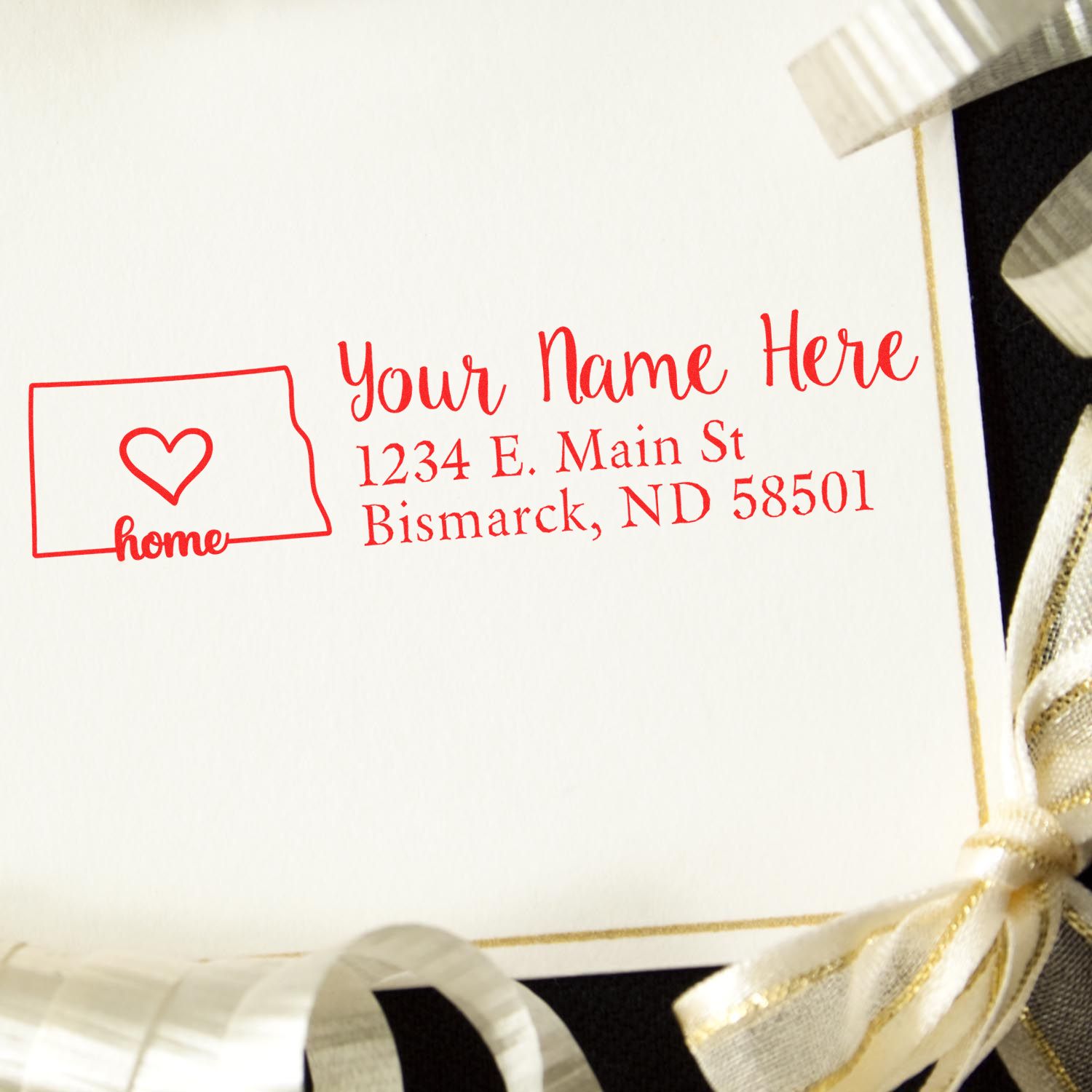 North Dakota Self-Inking State Love Address Stamp on an envelope, featuring a heart design and sample address in red ink, surrounded by gold ribbon.