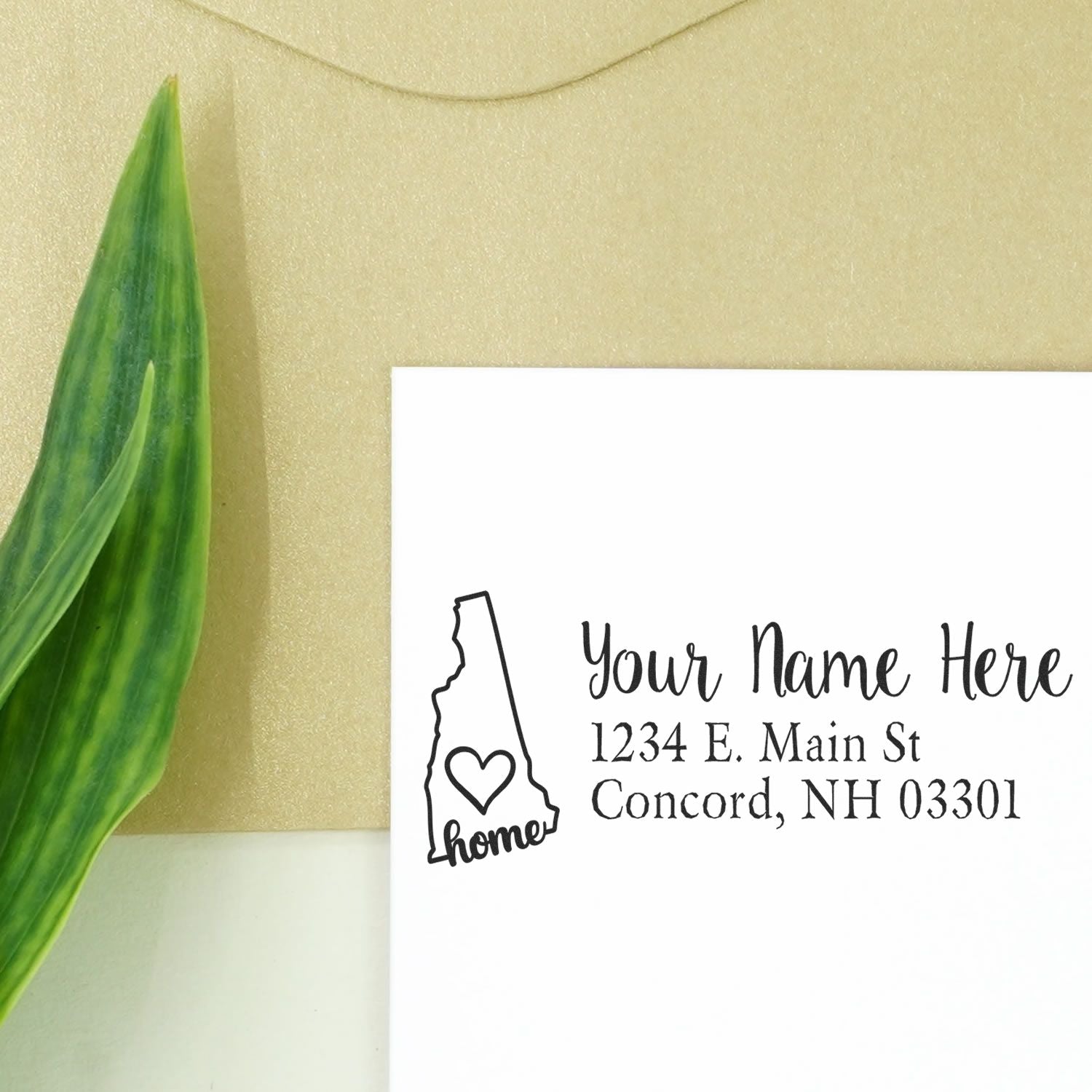 Wood Handle New Hampshire Custom Address Rubber Stamp on white paper with a heart design, next to a green leaf and beige envelope.