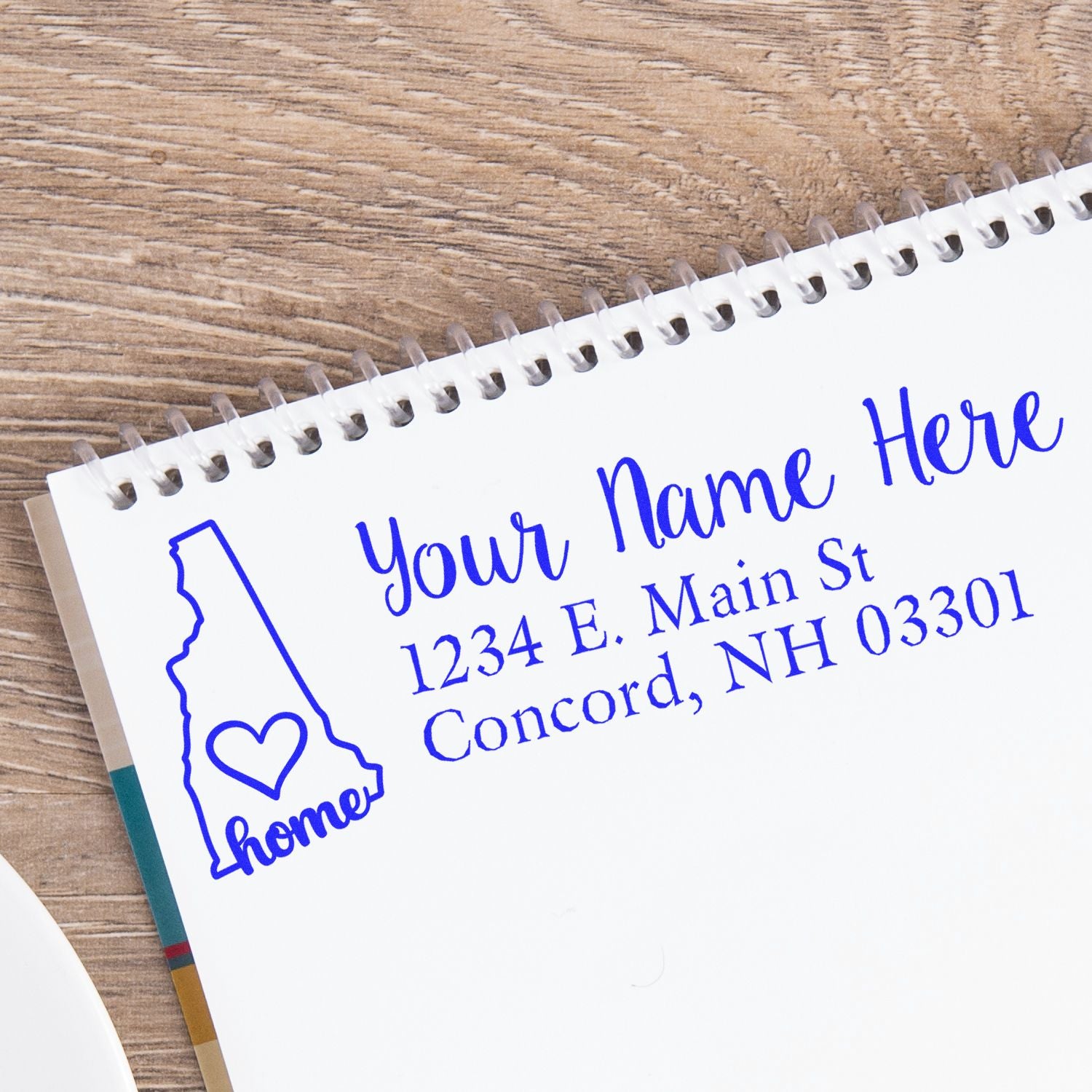 Wood Handle New Hampshire Custom Address Rubber Stamp on a notebook, featuring a blue imprint of a state outline with home text, personalized address, and elegant script.