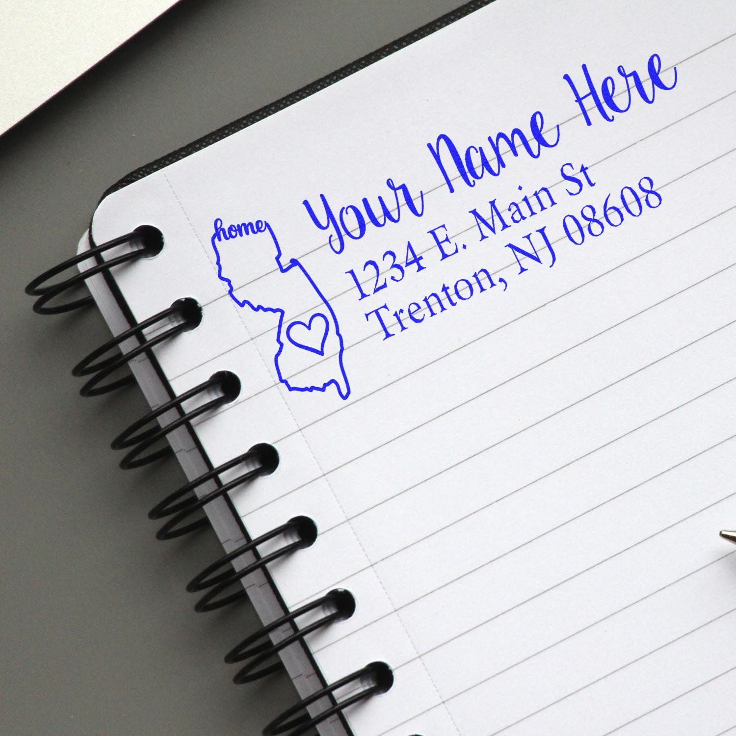 New Jersey Self-Inking State Love Address Stamp on a notebook page, featuring a blue outline of New Jersey with a heart and customizable address text.