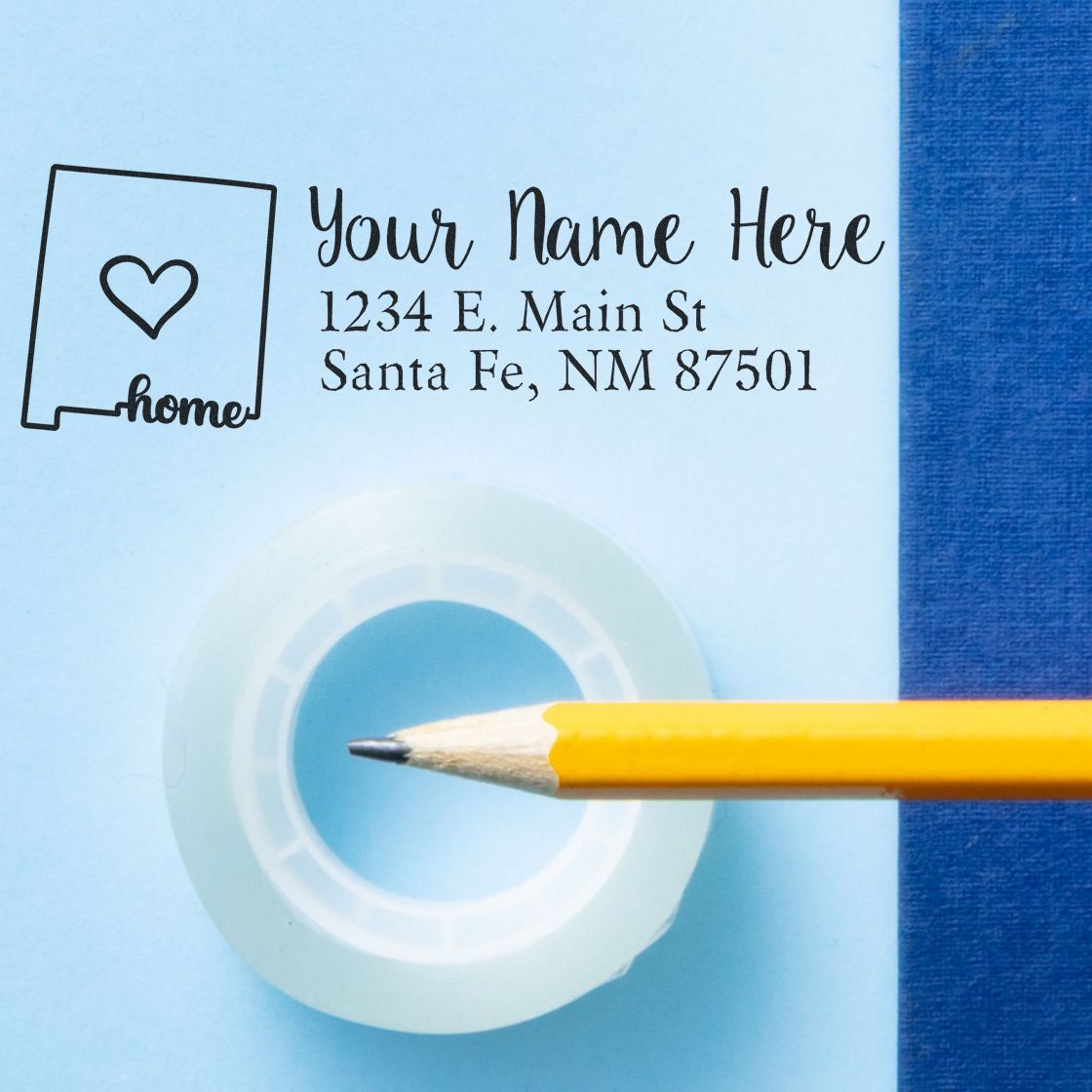 Wood Handle New Mexico Custom Address Rubber Stamp on blue paper, featuring a heart and state outline design. Includes sample address text with a pencil and tape nearby.