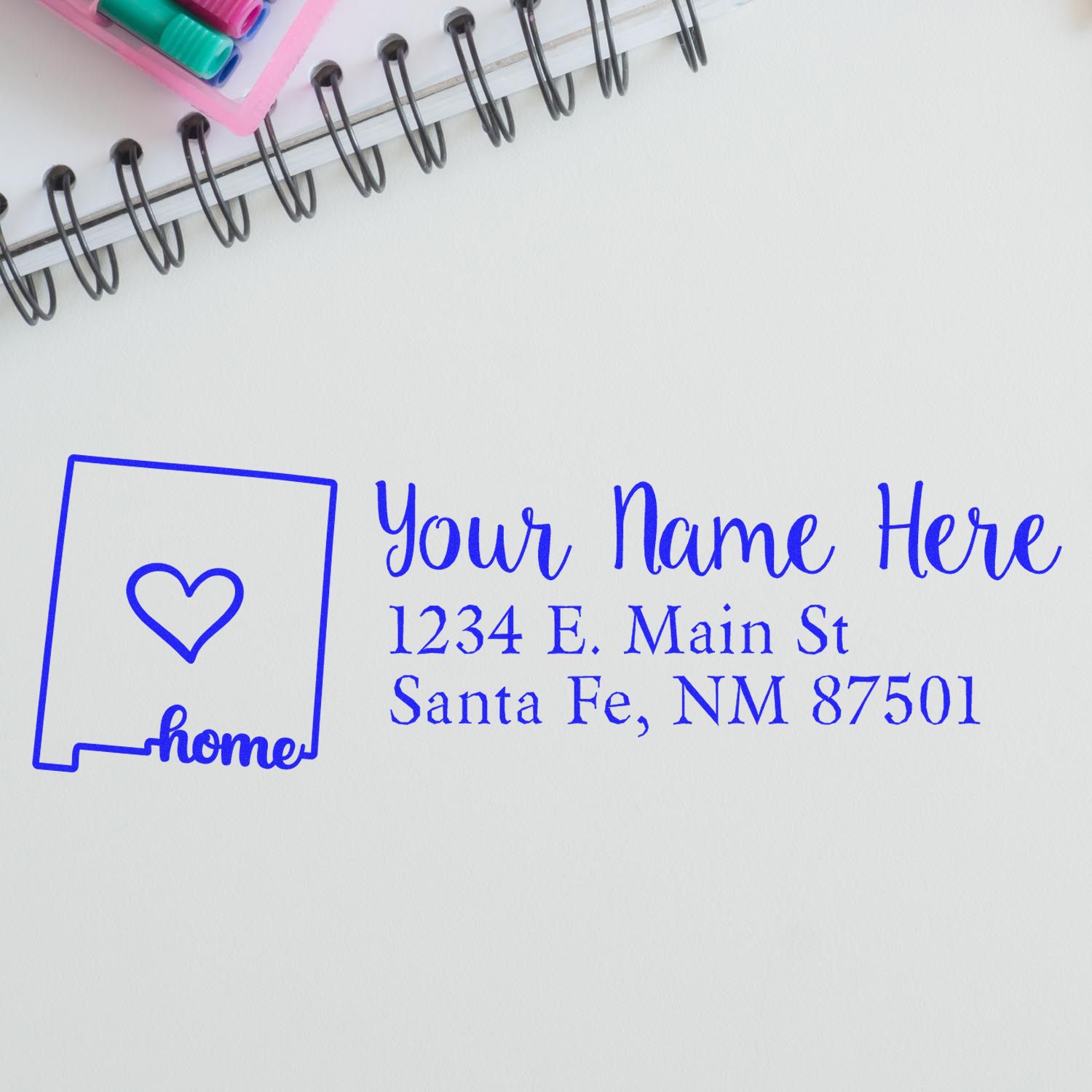 Wood Handle New Mexico Custom Address Rubber Stamp on paper with a heart design, showing Your Name Here and a Santa Fe address, next to a notebook and colored pens.