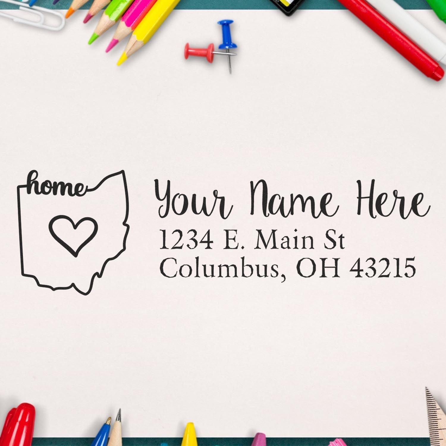 Ohio Self-Inking State Love Address Stamp on paper with Your Name Here and an Ohio outline with a heart. Surrounded by colorful pencils and pushpins. Perfect for personalized mail.