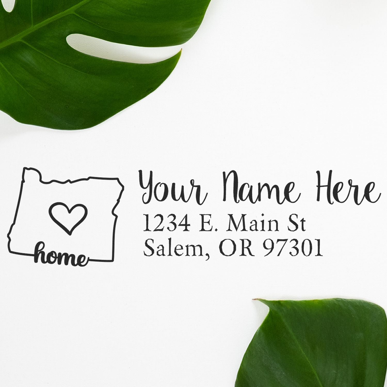 Oregon Self-Inking State Love Address Stamp on white paper with a heart inside the state outline, surrounded by green leaves. Text reads Your Name Here, 1234 E. Main St, Salem, OR 97301.