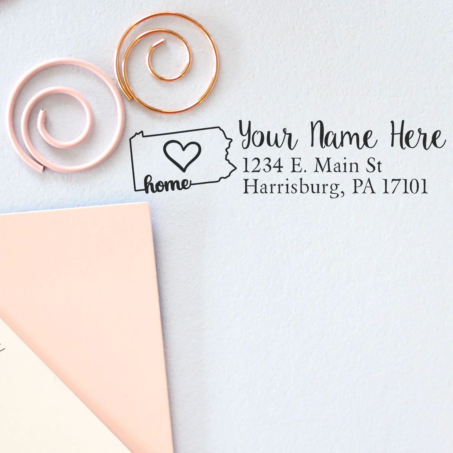 Wood Handle Pennsylvania Custom Address Rubber Stamp on paper with a heart design inside the state outline, next to pink and gold spiral paper clips.