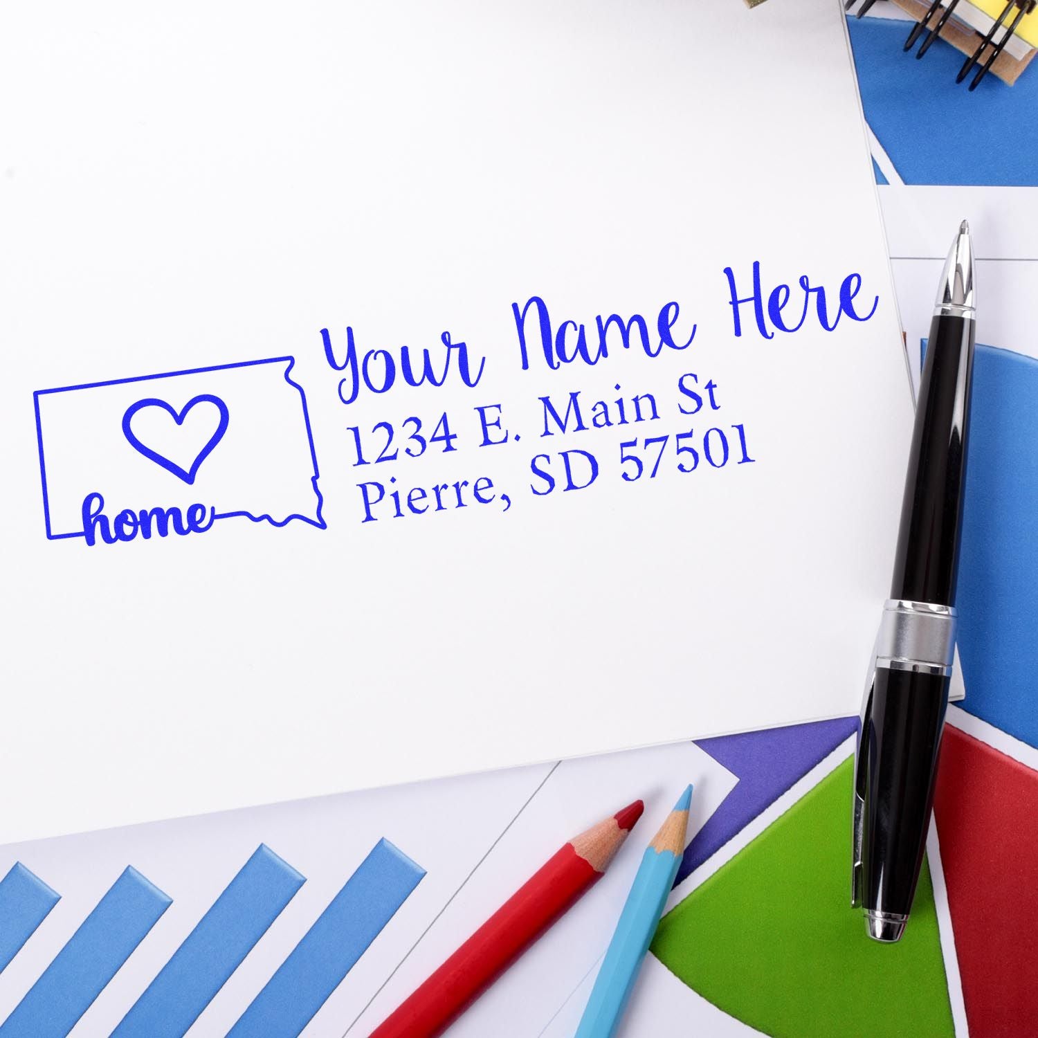 South Dakota Self-Inking State Love Address Stamp on white paper, featuring a heart and home text with a pen and colorful papers in the background.