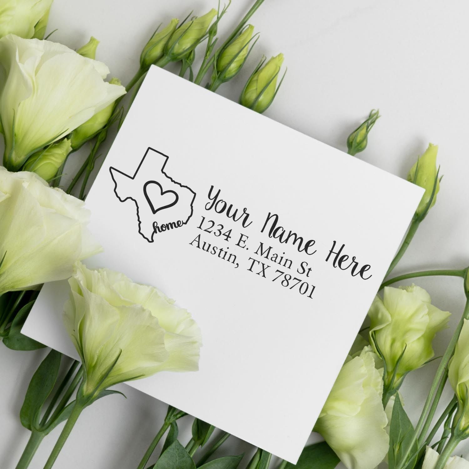 Slim Pre-Inked Texas State Love Custom Address Stamp on white envelope with green flowers. Features Texas outline with heart and customizable address text. Perfect for personalizing mail.