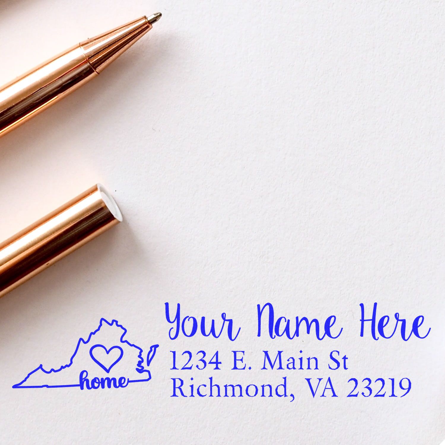 Slim Pre-Inked Virginia State Love Custom Address Stamp on white paper, featuring a blue outline of Virginia with home text, next to a rose gold pen.