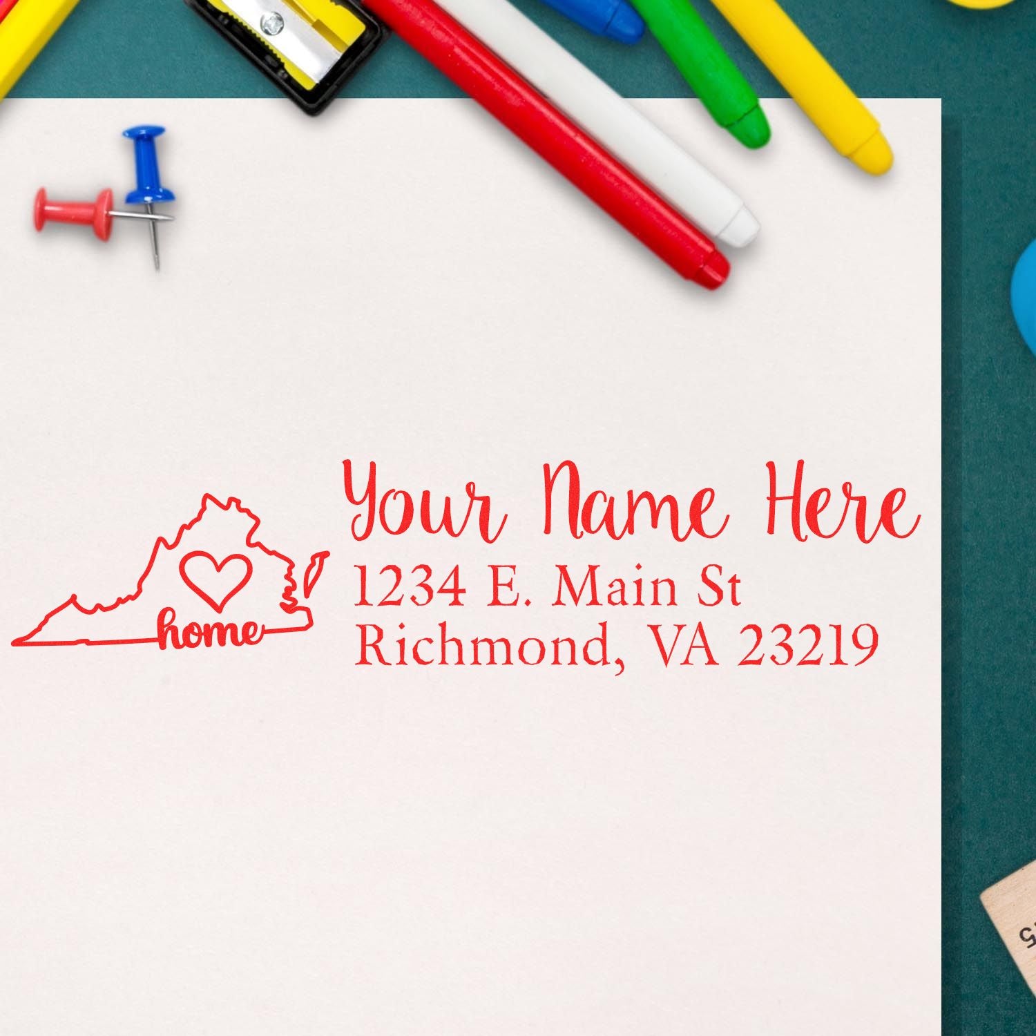 Slim Pre-Inked Virginia State Love Custom Address Stamp on white paper with red ink, featuring a Virginia outline and heart design. Surrounded by colorful pens and push pins.