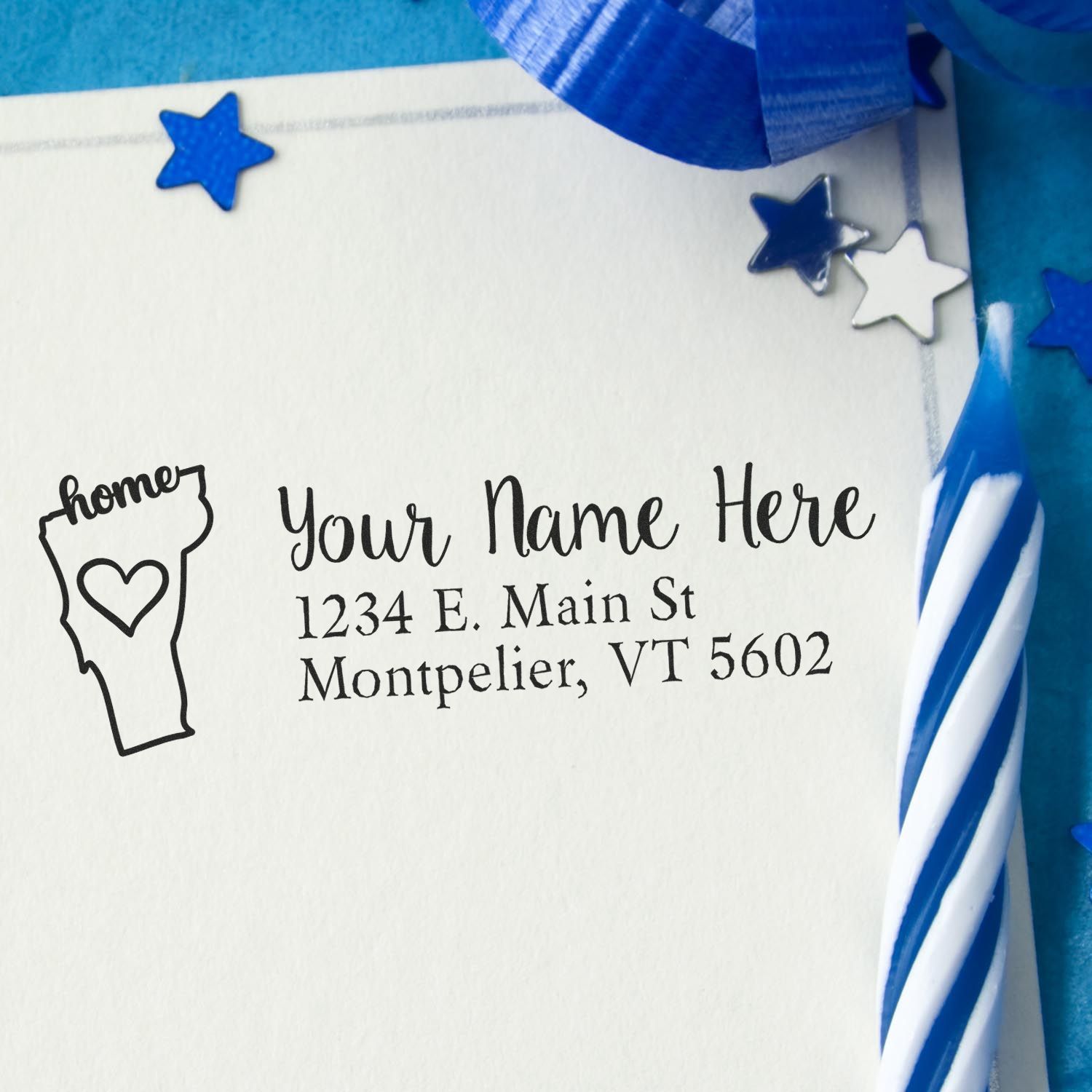 Wood Handle Vermont Custom Address Rubber Stamp on an envelope with a heart and home design, surrounded by blue stars and a striped candle, showcasing personalized address details.