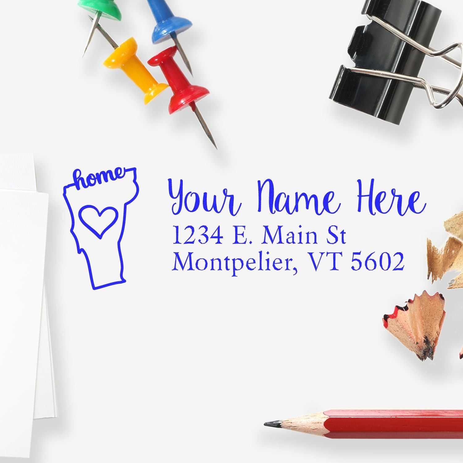 Wood Handle Vermont Custom Address Rubber Stamp on white paper, surrounded by colorful push pins, a binder clip, pencil shavings, and a red pencil, showcasing a personalized address design.