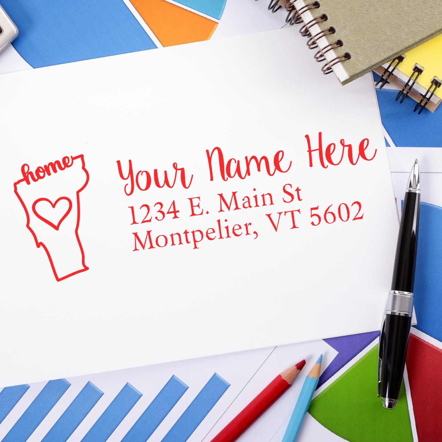 Vermont Self-Inking State Love Address Stamp on white paper with red ink, surrounded by colorful paper, a pen, and a notebook.