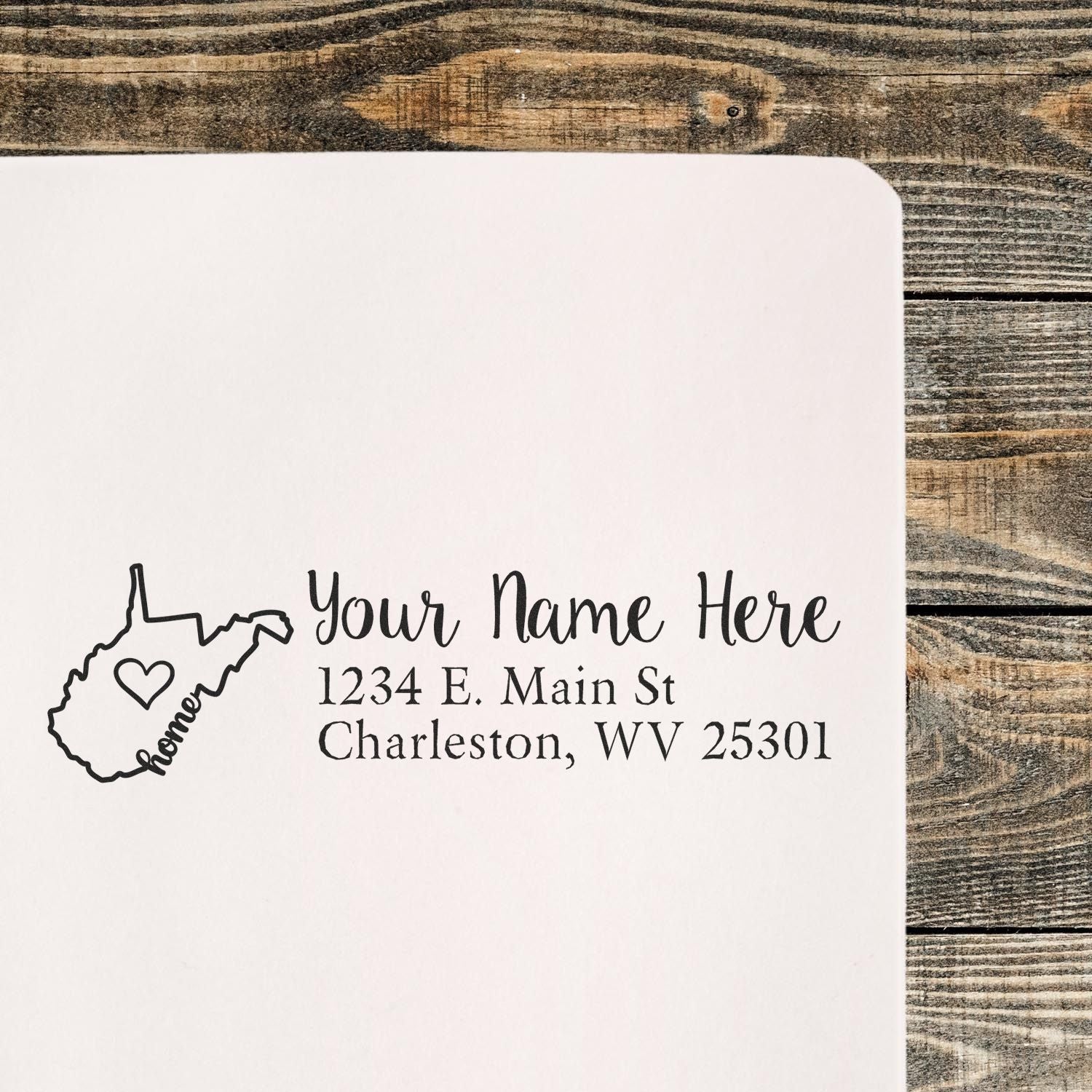 West Virginia Self-Inking State Love Address Stamp on paper, featuring a heart inside the state outline with home text, personalized with name and address. Rustic wooden background.