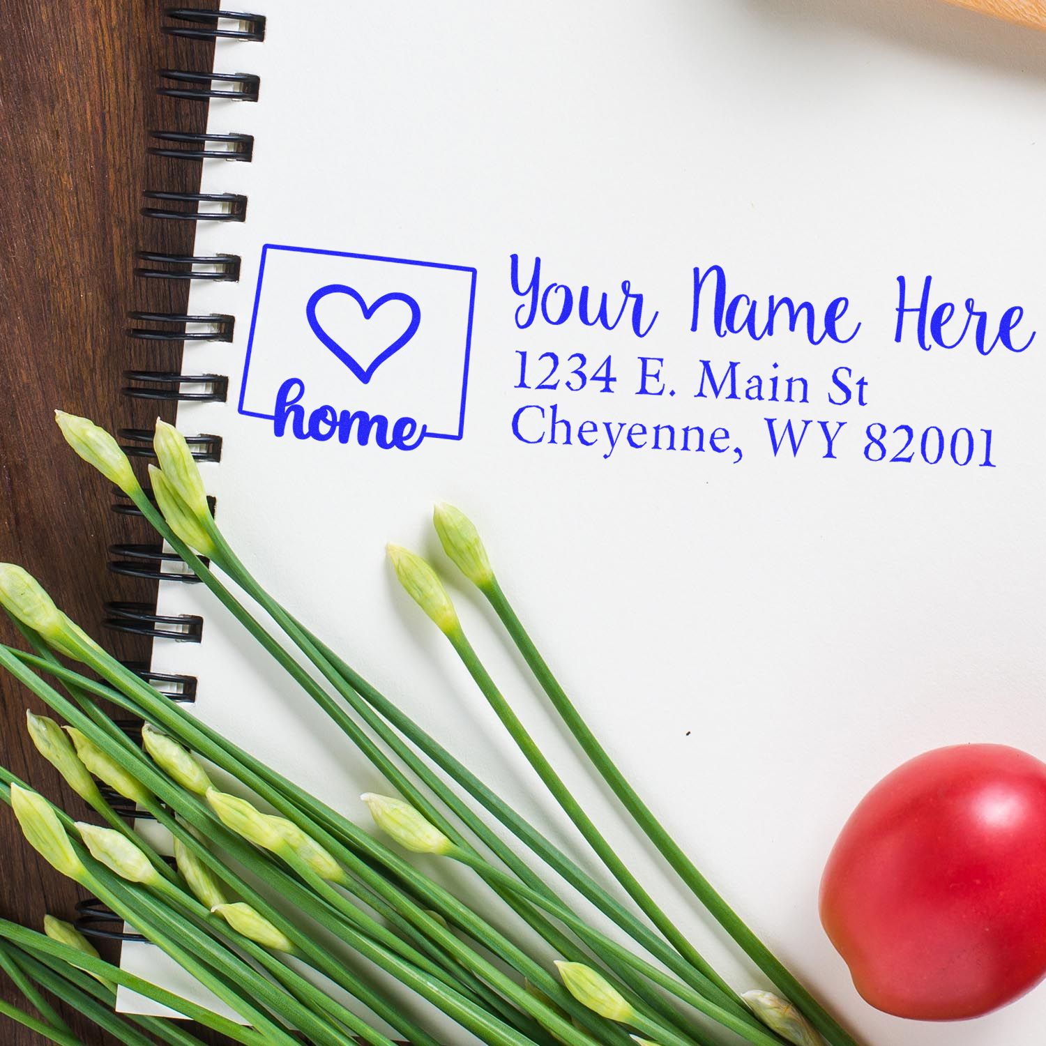 PSI Pre-Inked Personalized Wyoming State Love Address Stamp on a notepad with a heart design, surrounded by green stems and a red tomato, showcasing a sample address in blue ink.