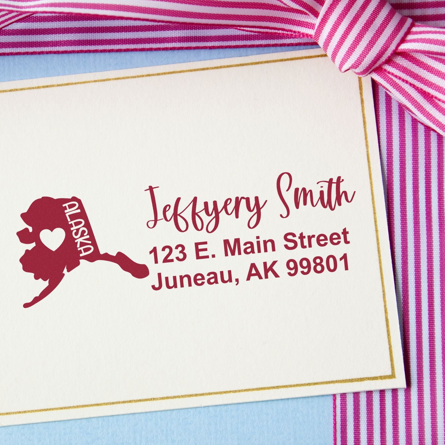 Alaska State Love Personalized Address Stamp on a card with a pink striped ribbon. Features a red Alaska map with a heart, personalized with name and address in elegant script.