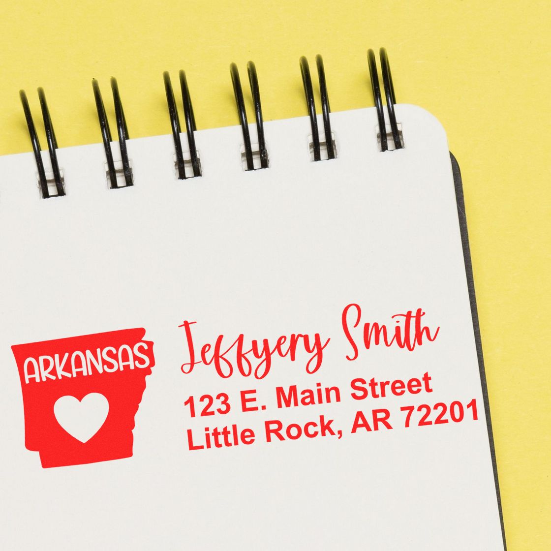 State Love of Arkansas Custom Address Stamp Self-Inking on a notepad, featuring a red Arkansas state outline with a heart and personalized address in red text.