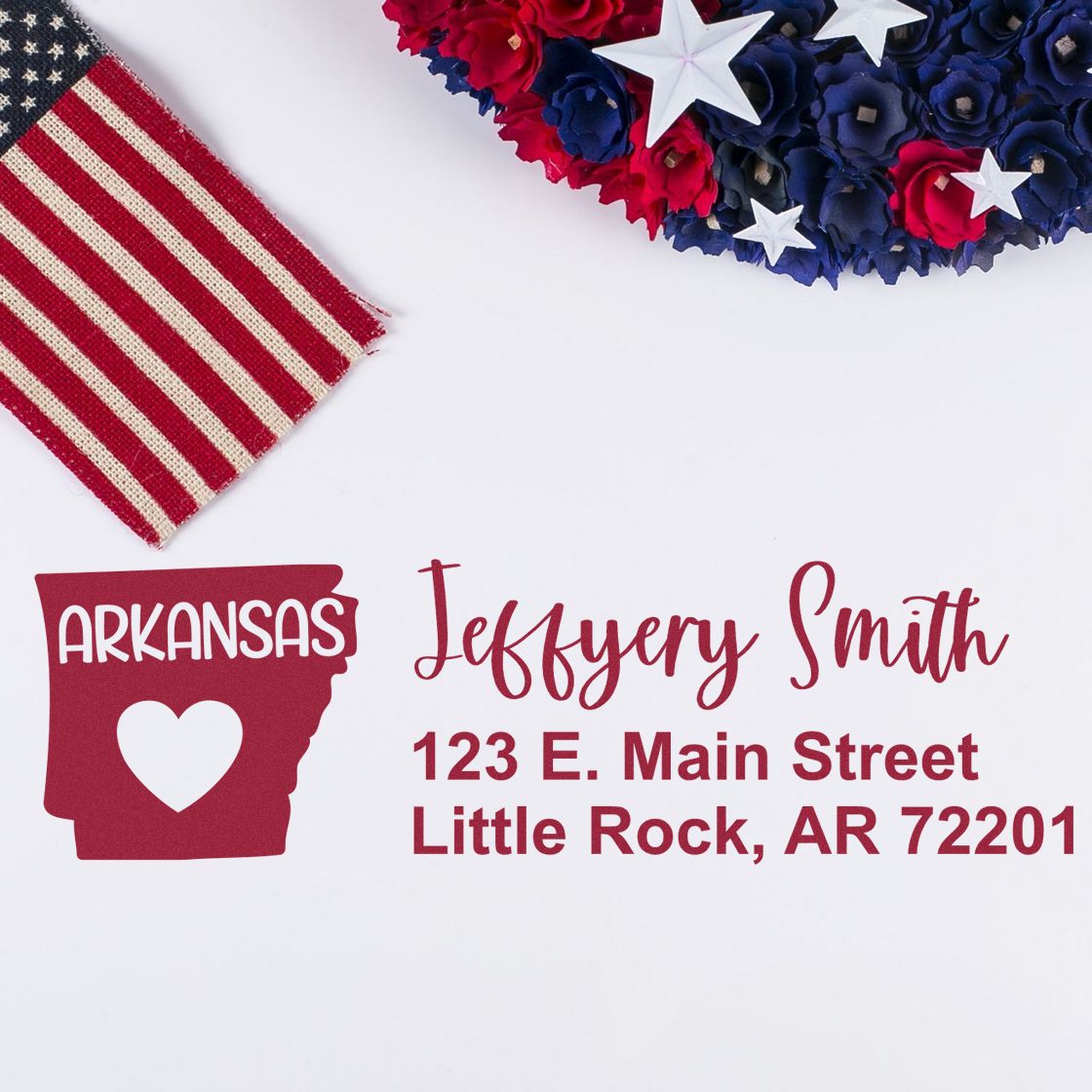 PSI Pre-Inked Arkansas State Love Customized Address Stamp displayed on paper with a heart design, next to a decorative American flag and floral arrangement.