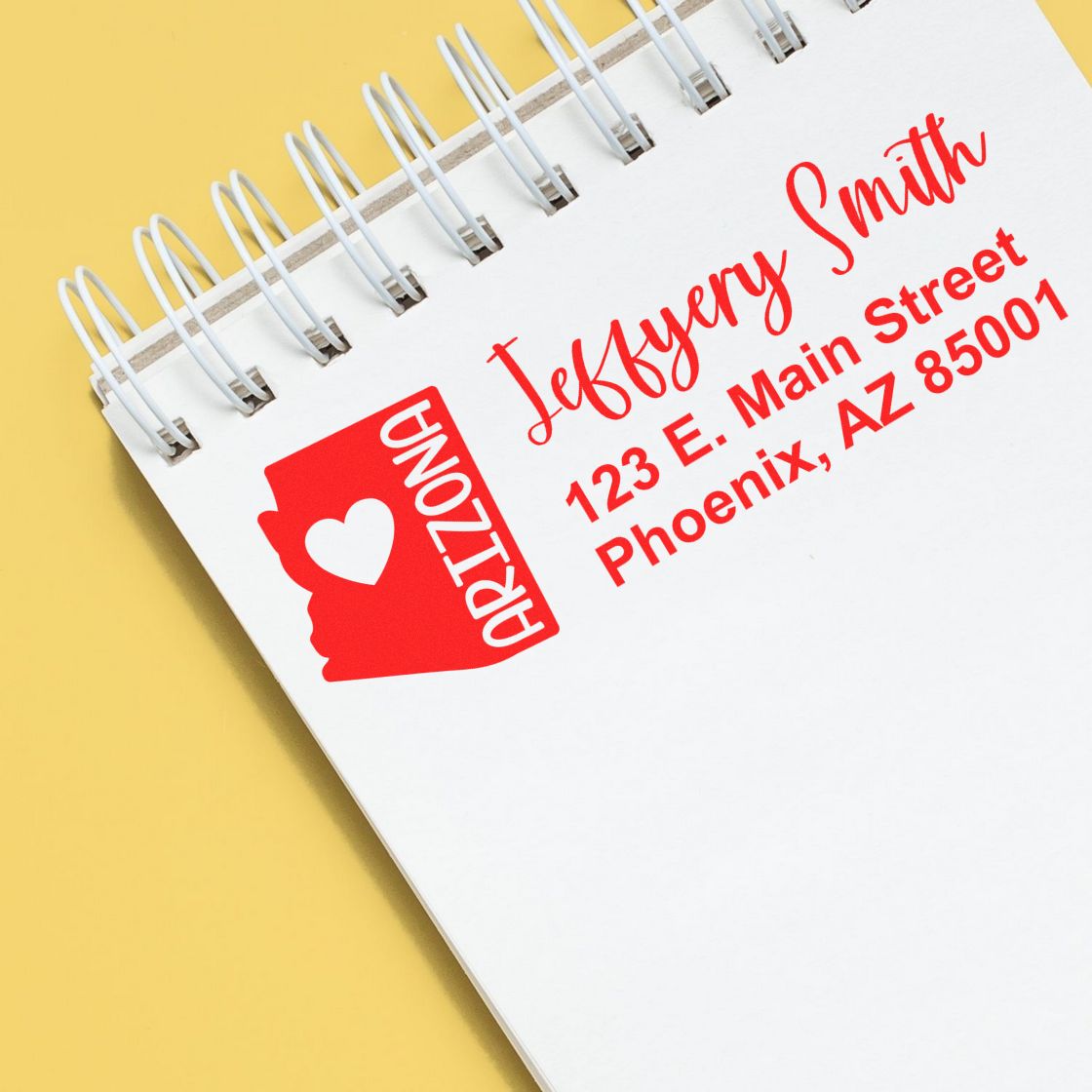 Image of a notebook with a red Arizona State Love Personalized Address Stamp imprint, featuring a heart and the text Jeffery Smith, 123 E. Main Street, Phoenix, AZ 85001 on a yellow background.