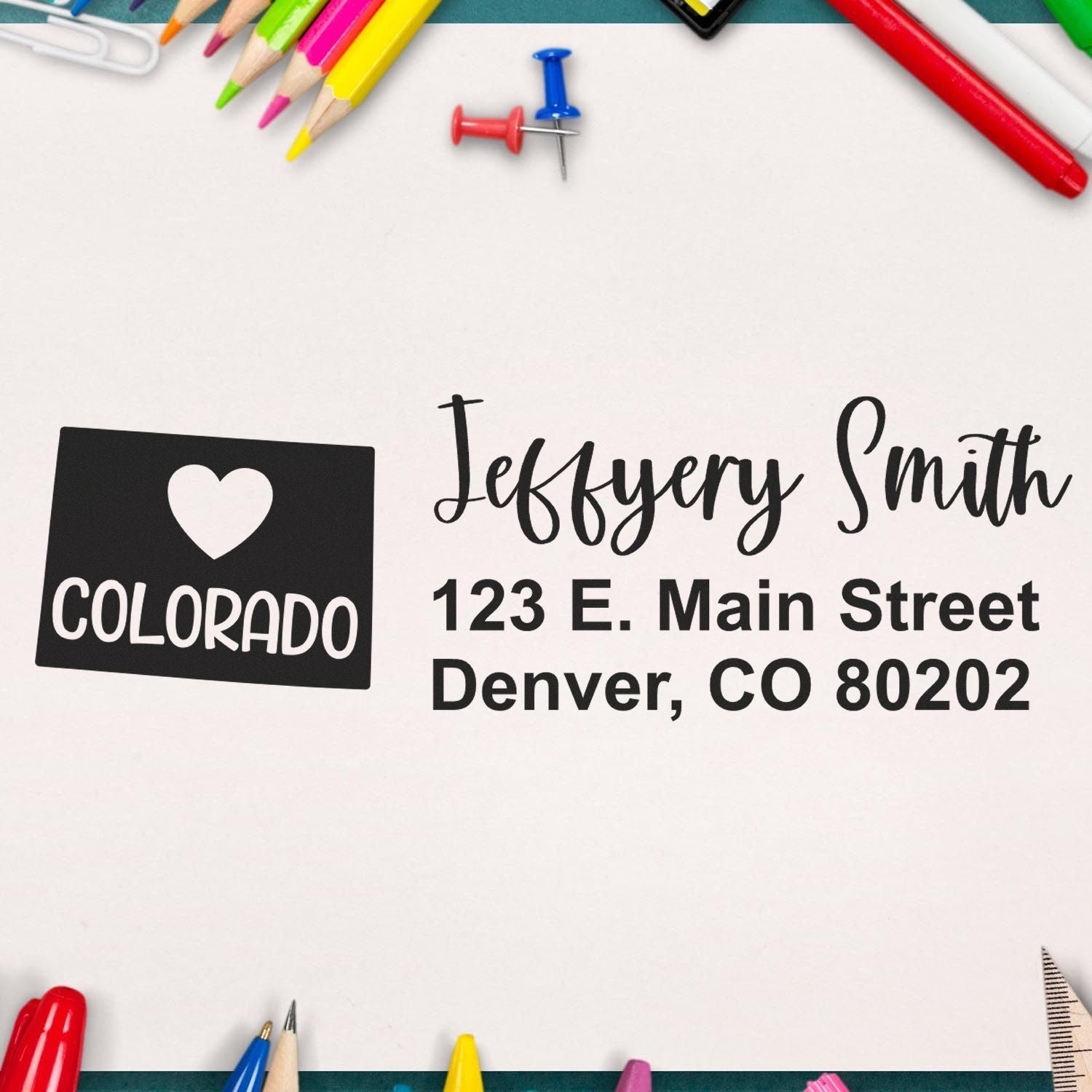 PSI Pre-Inked Colorado State Love Customized Address Stamp on paper with Jeffery Smith, 123 E. Main Street, Denver, CO 80202 surrounded by colorful stationery items.