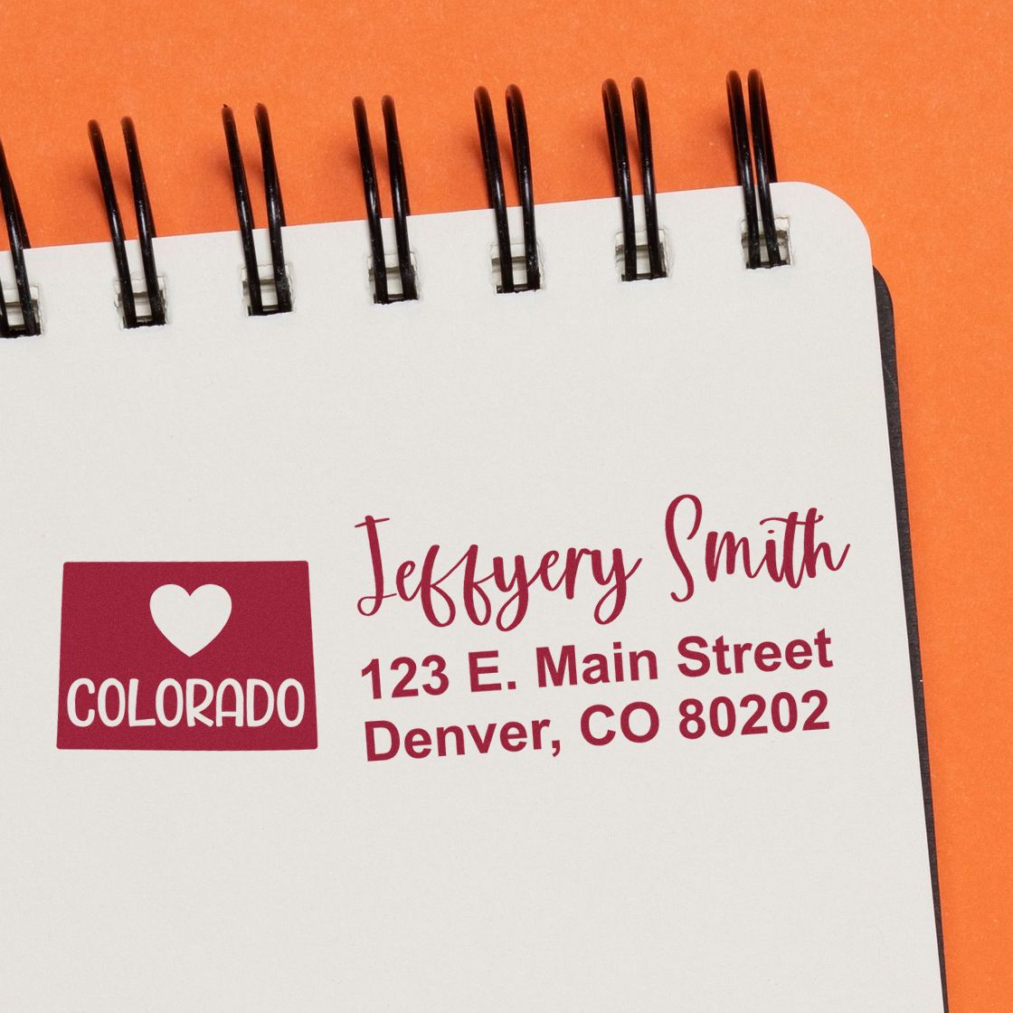 State Love of Colorado Custom Address Stamp Self-Inking on a notepad, featuring a heart and Colorado design with a sample address in red ink against an orange background.