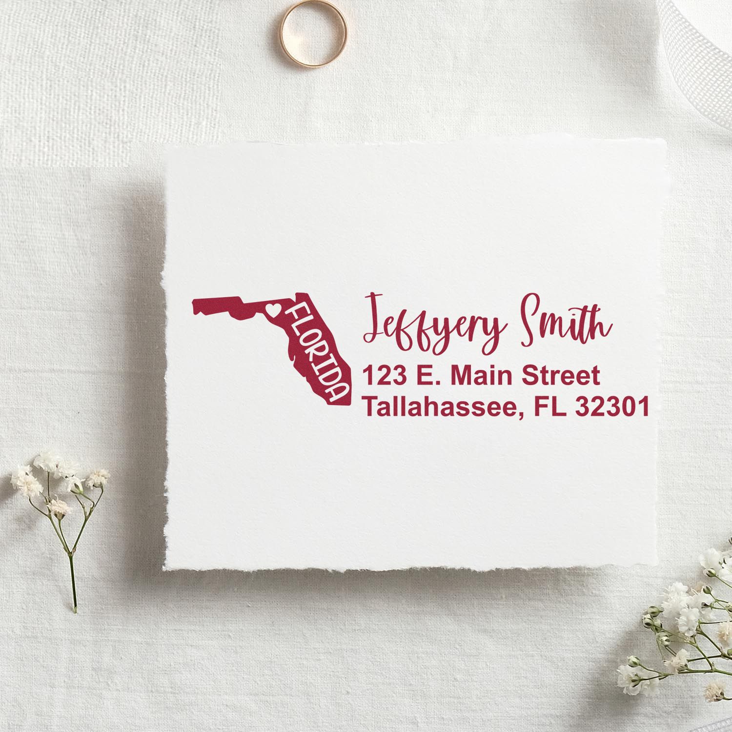 PSI Pre-Inked Florida State Love Customized Address Stamp on white paper with red ink, featuring a Florida map design and personalized address. Set on a textured surface with small flowers and a ring.