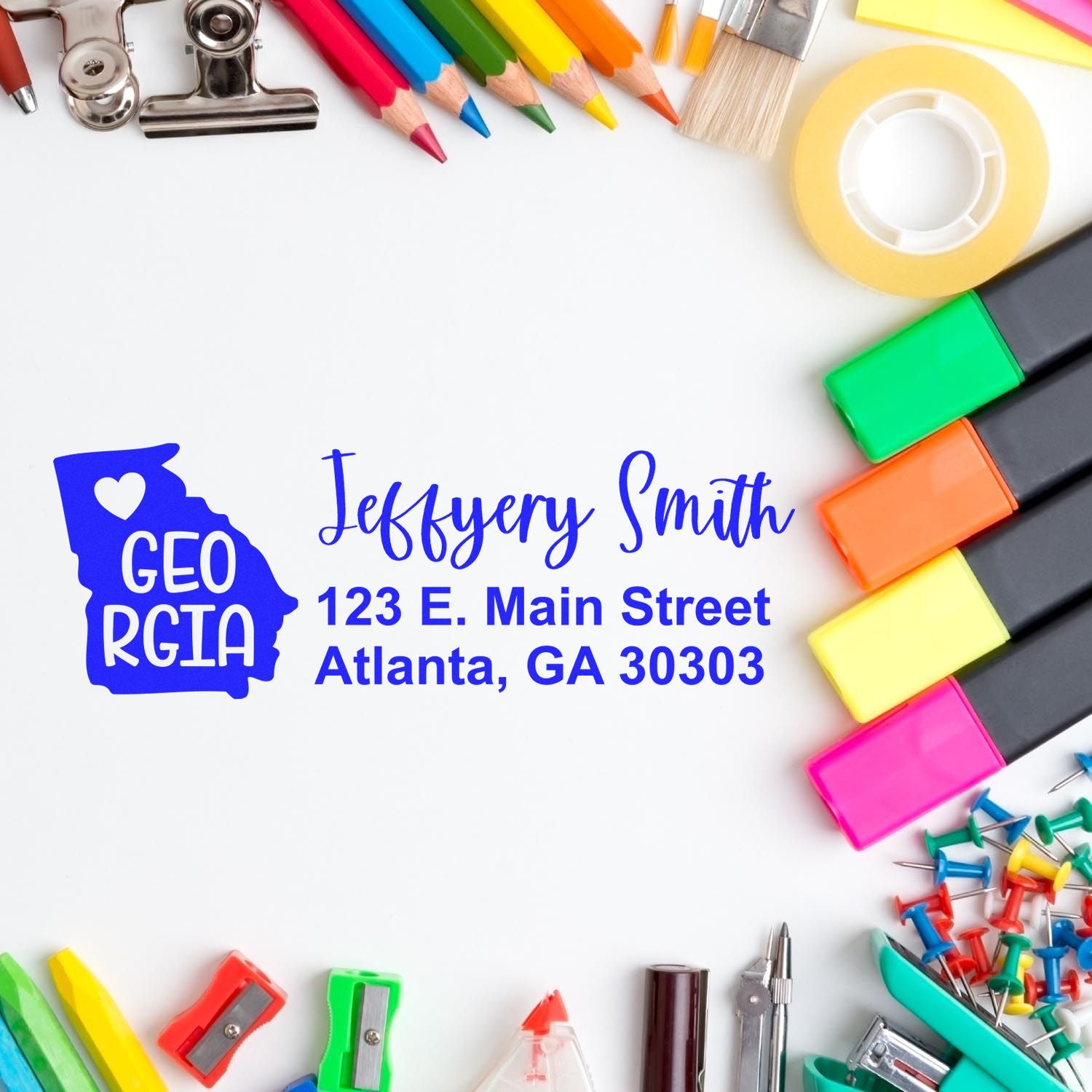 Georgia State Love Personalized Address Stamp on a desk surrounded by colorful office supplies, featuring a heart design and sample address for Jeffery Smith, 123 E. Main Street, Atlanta, GA 30303.