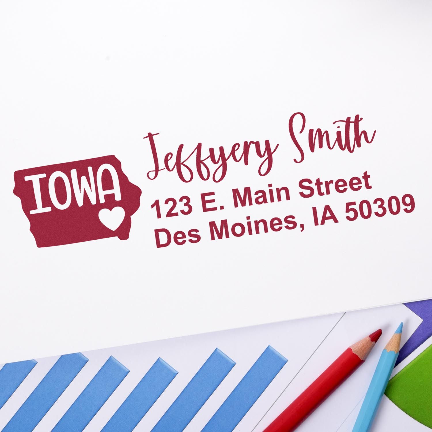 Iowa State Love Personalized Address Stamp on white paper with red ink, featuring a heart and state outline, next to colored pencils and a striped folder.