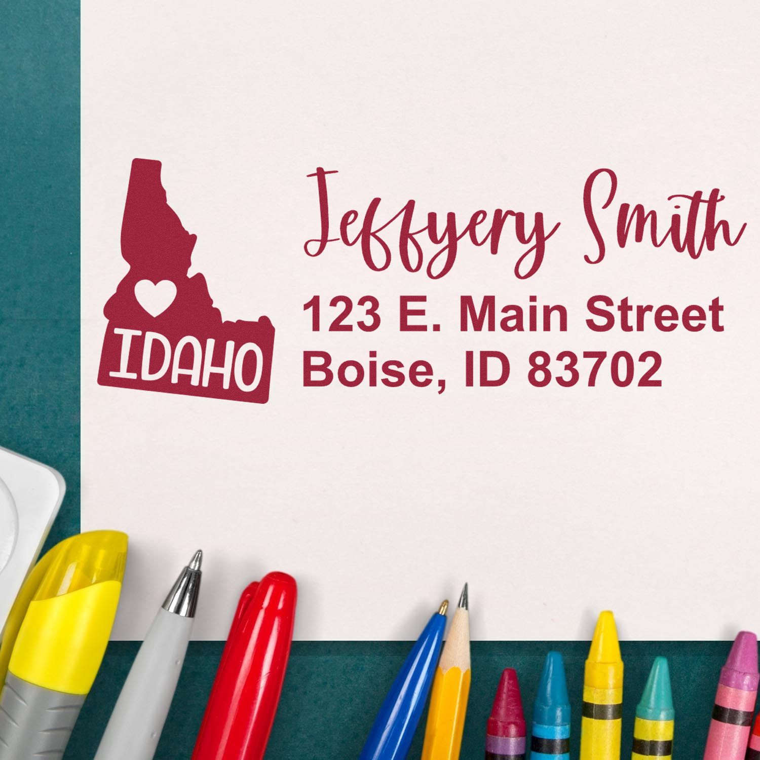 Slim Idaho Custom Address Stamp for Envelopes displayed on white paper with colorful pens. Features a red Idaho state outline with heart, personalized with name and address in bold, stylish font.