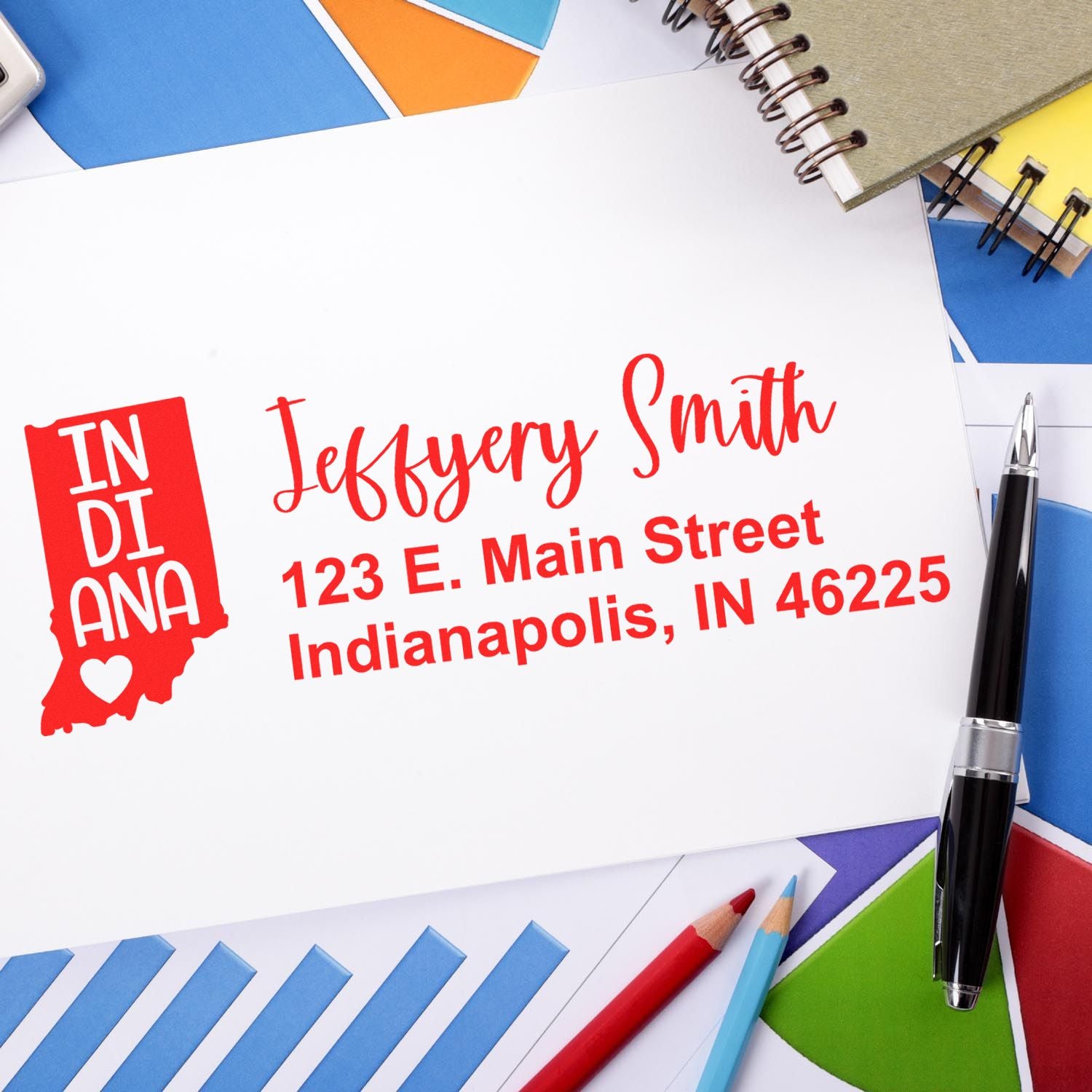 Slim Indiana Custom Address Stamp for Envelopes displayed on a white envelope with red text, surrounded by colorful stationery and a pen.