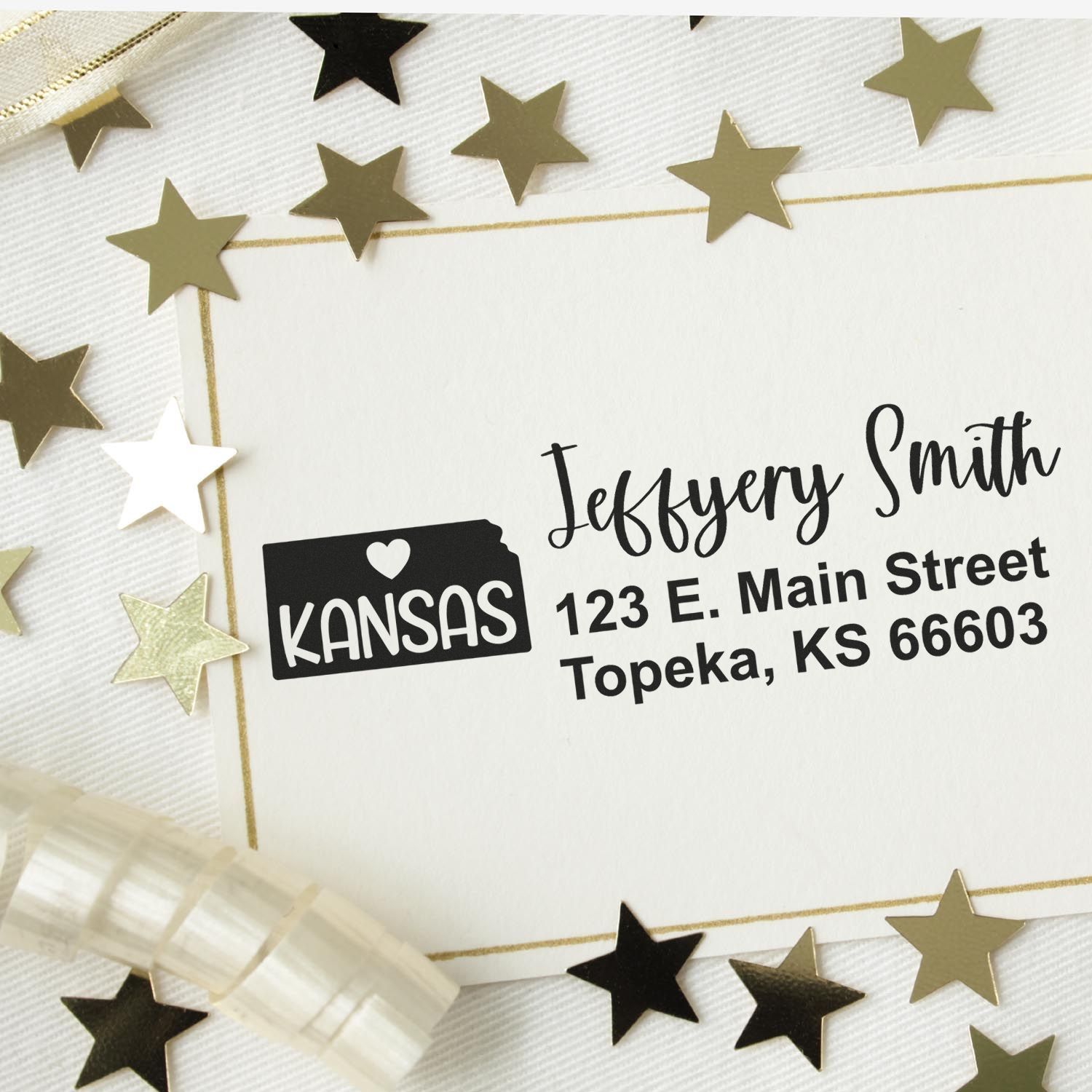 Image of a PSI Pre-Inked Kansas State Love Customized Address Stamp on an envelope, featuring a Kansas state outline with a heart, surrounded by gold stars and ribbon.