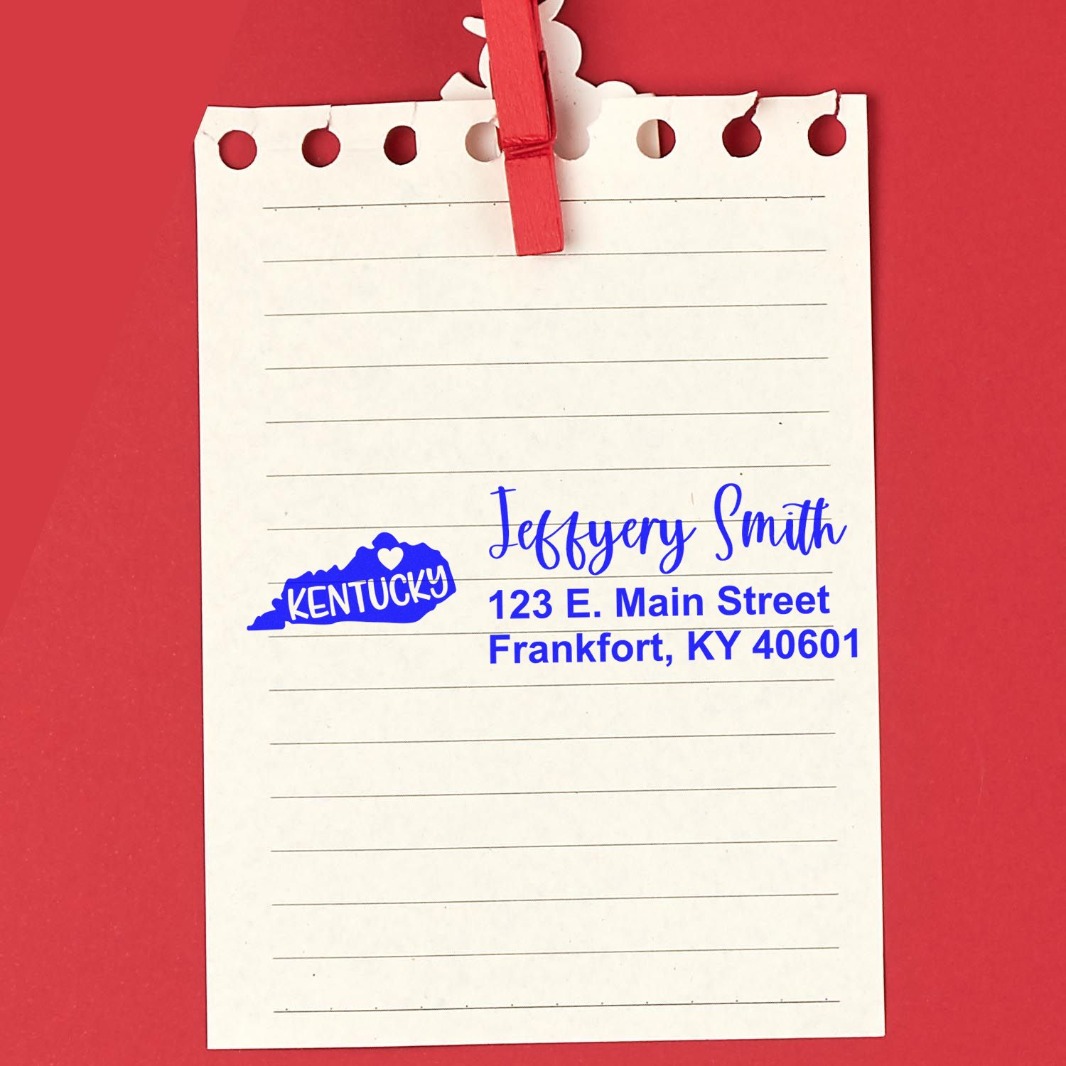 Kentucky State Love Personalized Address Stamp on a notepad with a red background. The stamp features a blue Kentucky state outline with a heart, personalized with a name and address in blue ink.