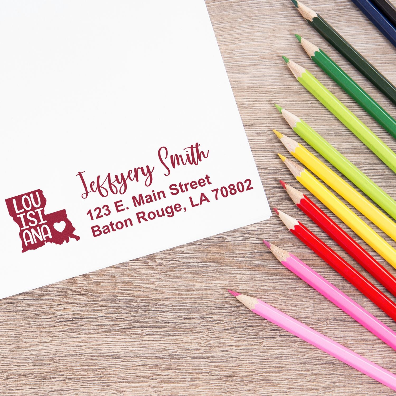 Slim Louisiana Custom Address Stamp for Envelopes on white paper, featuring a red Louisiana state design and address. Colored pencils are arranged nearby on a wooden surface.