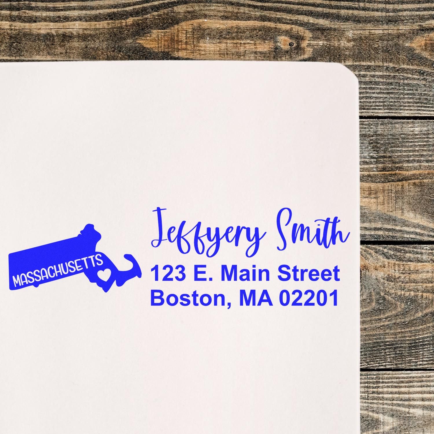 Massachusetts State Love Personalized Address Stamp on white paper, featuring a blue state outline with a heart and custom address text, placed on a wooden surface.