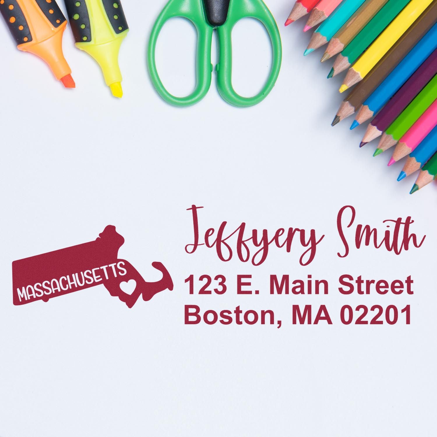 Massachusetts State Love Personalized Address Stamp on a white surface with colorful pencils and scissors. The stamp features a red Massachusetts outline with a heart, personalized with an address.