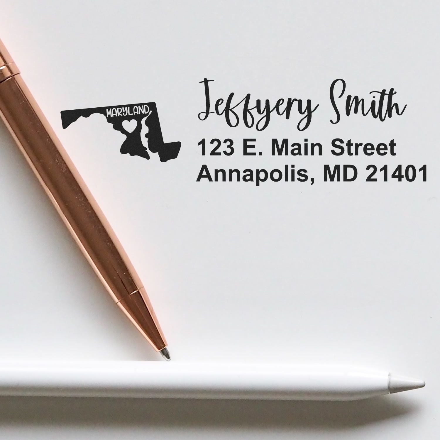 Maryland State Love Personalized Address Stamp featuring a Maryland map with a heart, next to a rose gold pen and a white pencil on a white background.