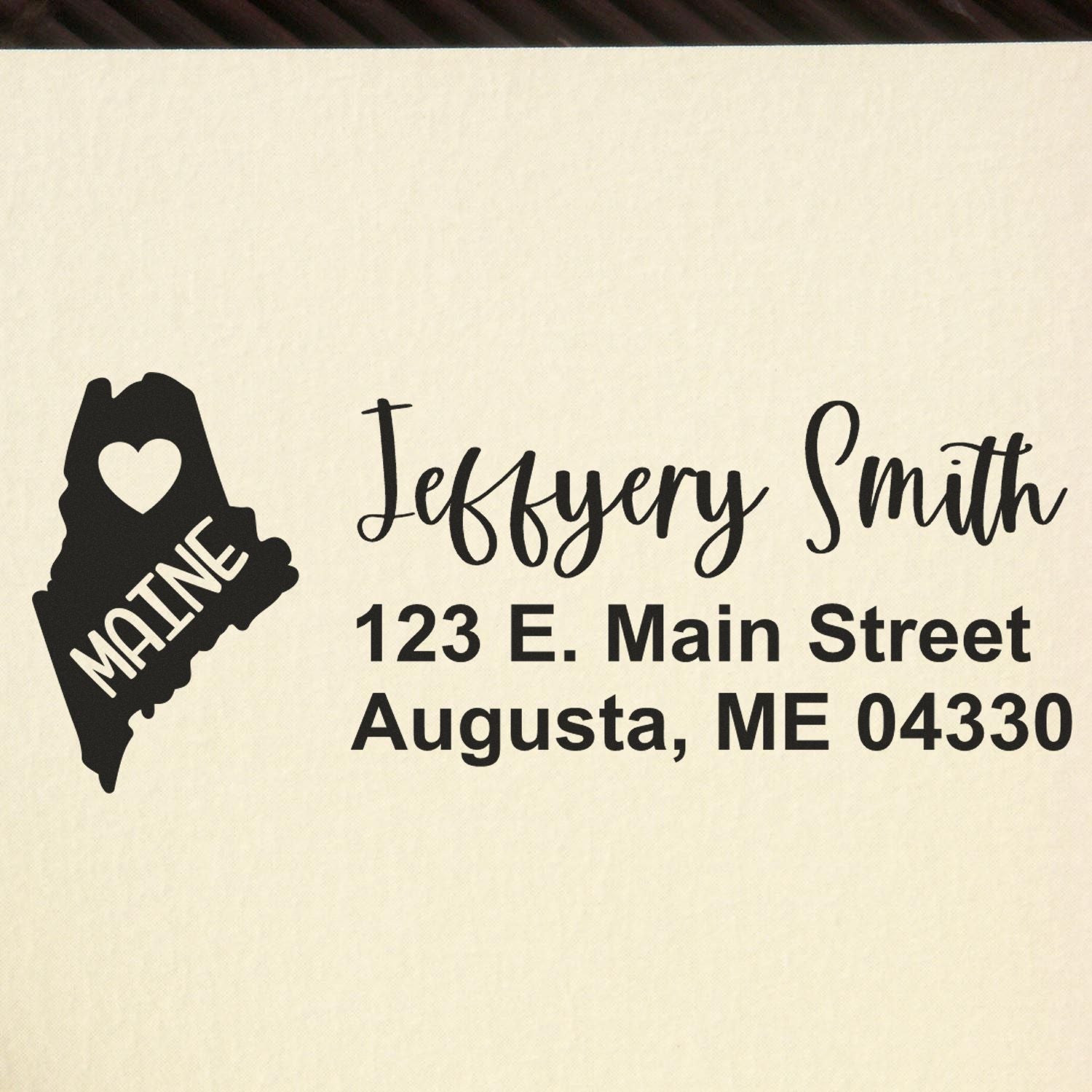 Image of the State Love of Maine Custom Address Stamp Self-Inking, featuring a heart within the state outline and personalized address text: Jeffery Smith, 123 E. Main Street, Augusta, ME 04330.