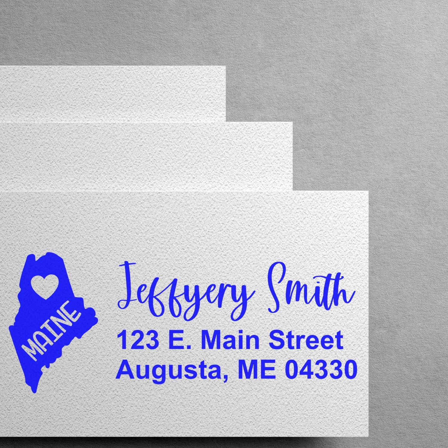 State Love of Maine Custom Address Stamp Self-Inking on white envelopes, featuring a blue Maine state outline with a heart and personalized address in blue text.