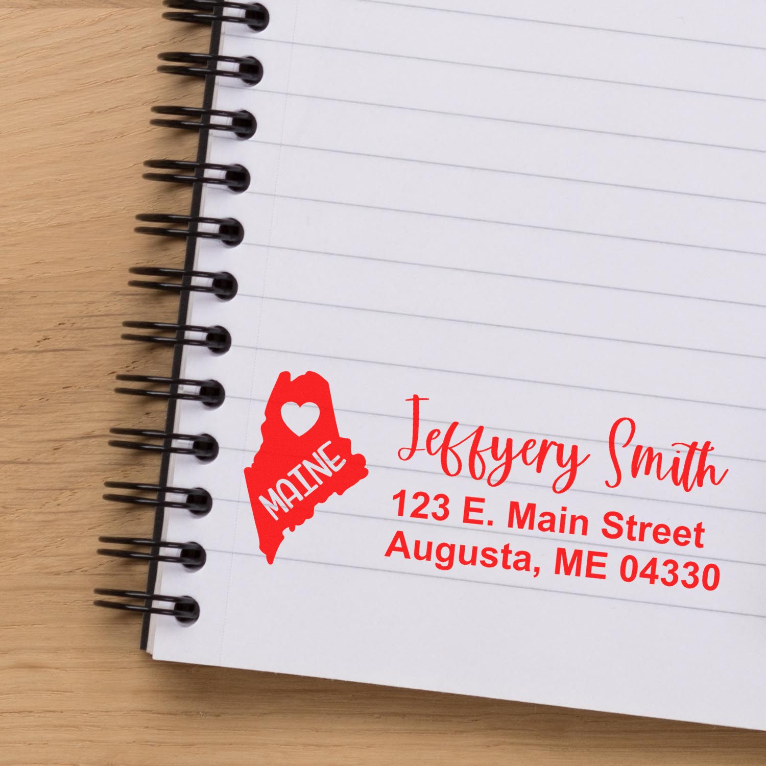 PSI Pre-Inked Maine State Love Customized Address Stamp on a notebook, featuring a red Maine state outline with a heart and personalized address in red ink.