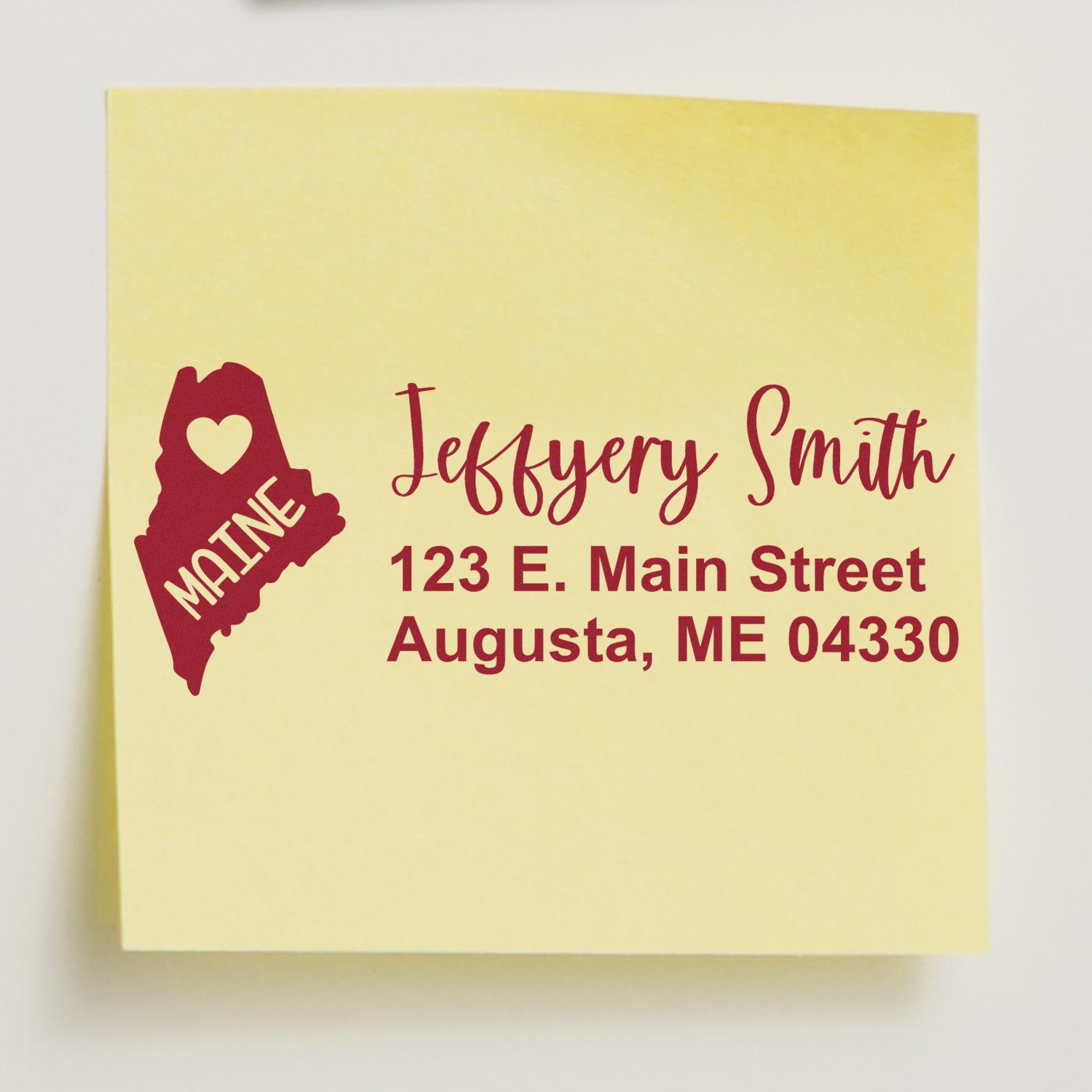 State Love of Maine Custom Address Stamp Self-Inking displayed on a yellow paper, featuring a heart and the word Maine with a sample address in red text.