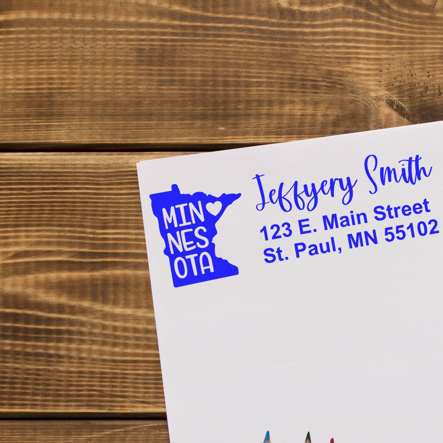 Envelope stamped with State Love of Minnesota Custom Address Stamp Self-Inking, featuring a blue Minnesota state outline and address in elegant font on a wooden surface.