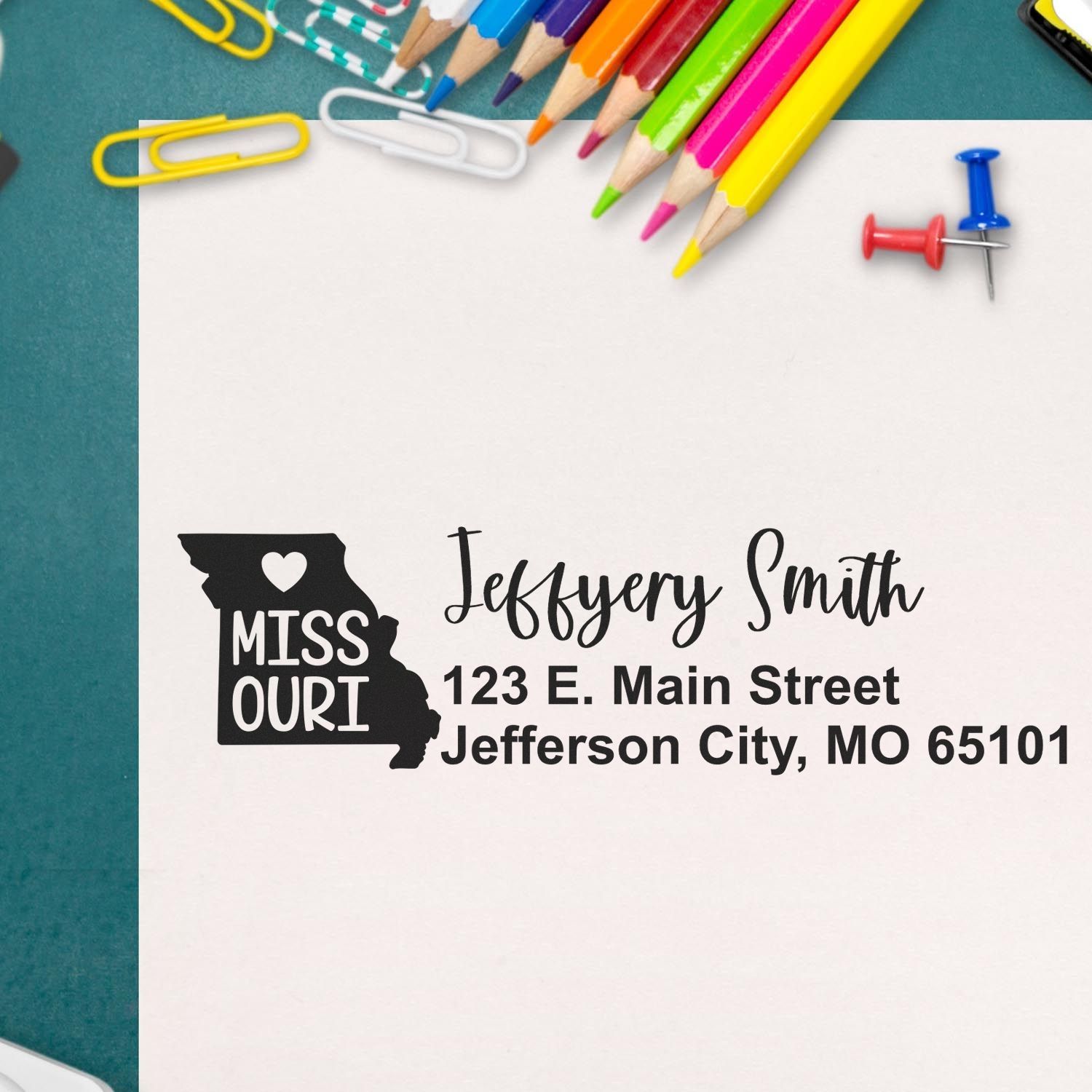 PSI Pre-Inked Missouri State Love Customized Address Stamp on paper with colorful pencils and paperclips. Features Missouri map design with heart and personalized address details.